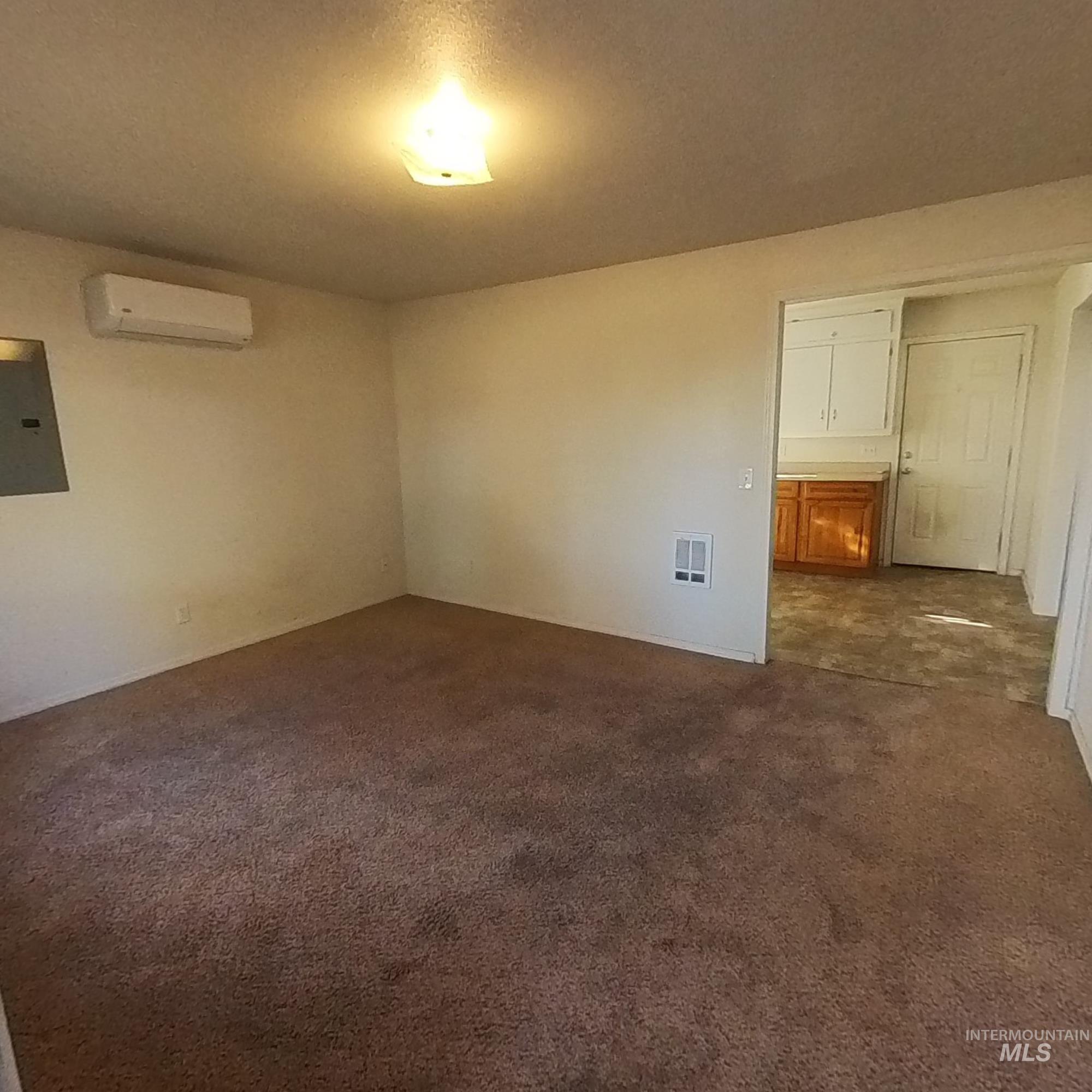 Spare room featuring dark carpet, electric panel, and an AC wall unit