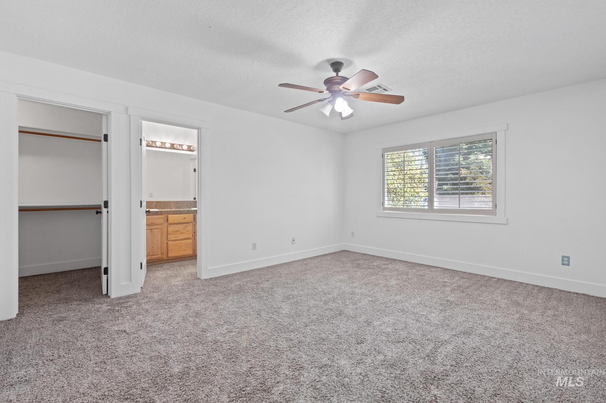 Unfurnished bedroom featuring light carpet, a textured ceiling, a ceiling fan, a walk in closet, and ensuite bathroom