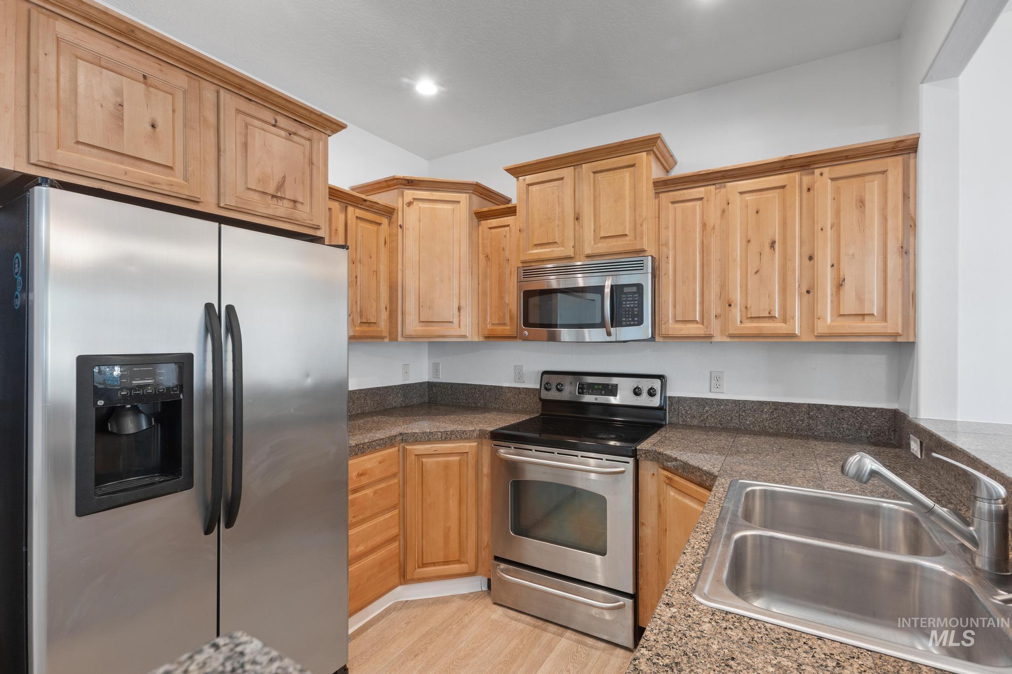 Kitchen with stainless steel appliances, tile countertops, light brown cabinetry, light wood finished floors, and recessed lighting