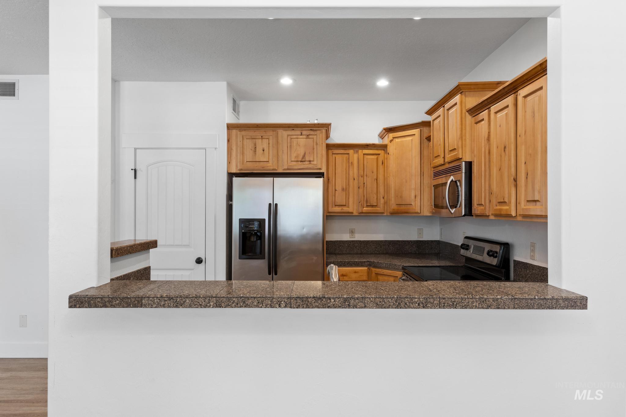 Kitchen featuring tile countertops, stainless steel appliances, brown cabinetry, recessed lighting, and wood finished floors