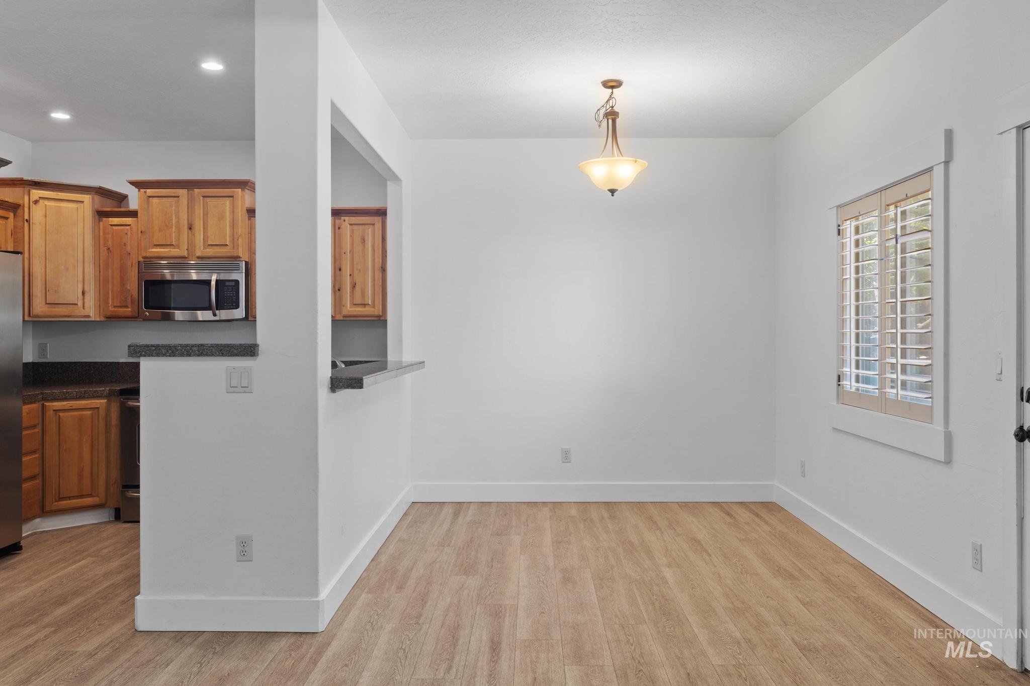 Kitchen with light wood-type flooring, stainless steel microwave, hanging light fixtures, brown cabinets, and recessed lighting