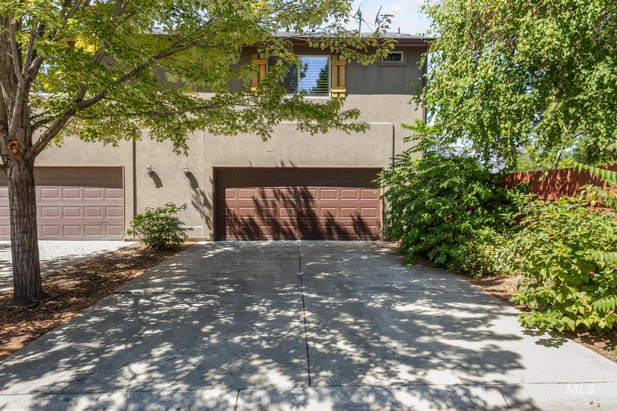 View of property hidden behind natural elements featuring stucco siding, a garage, and driveway