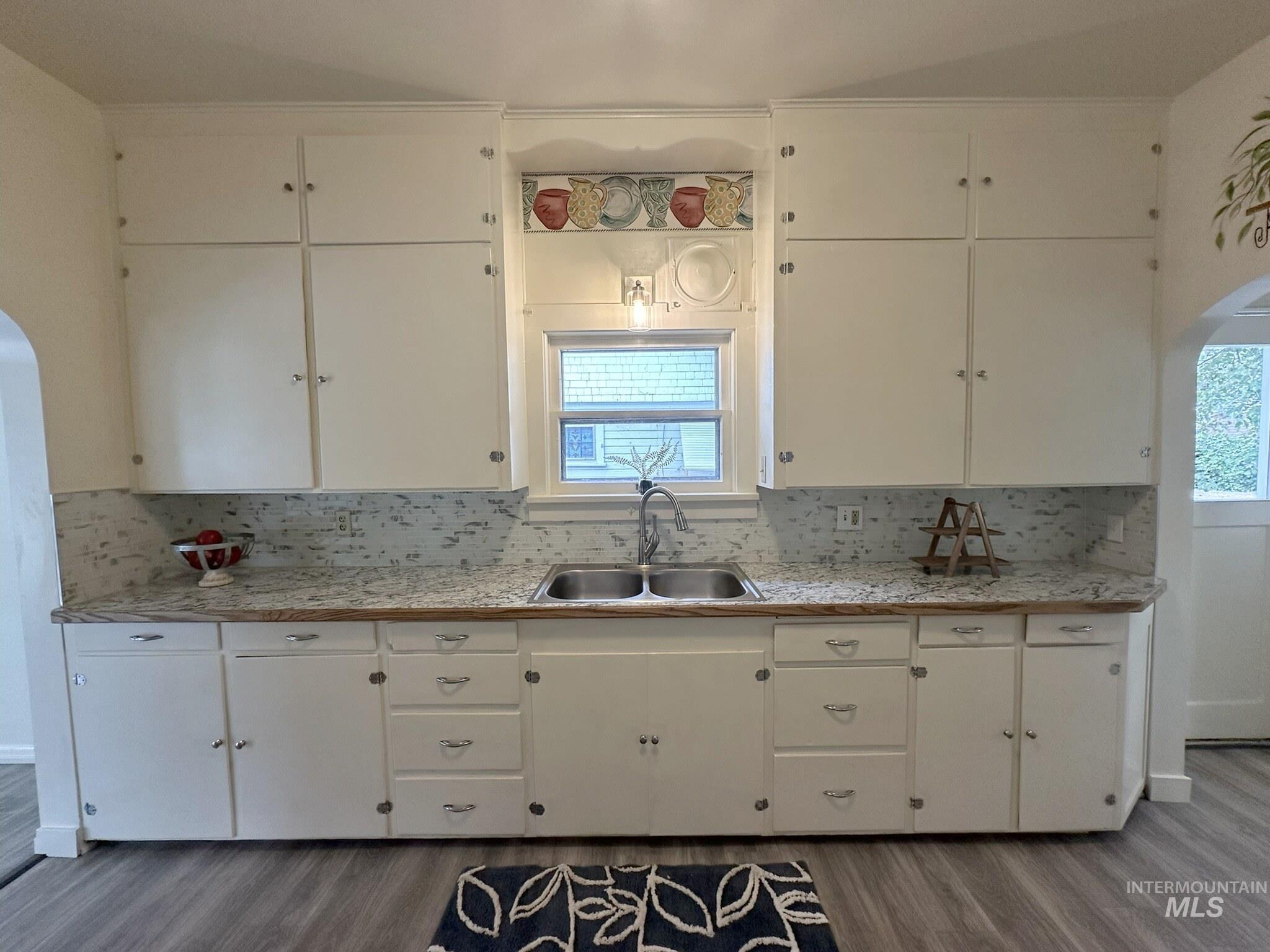 Kitchen featuring extensive white cabinetry, a double basin stainless steel sink, light-toned countertops, and a full-height tile backsplash