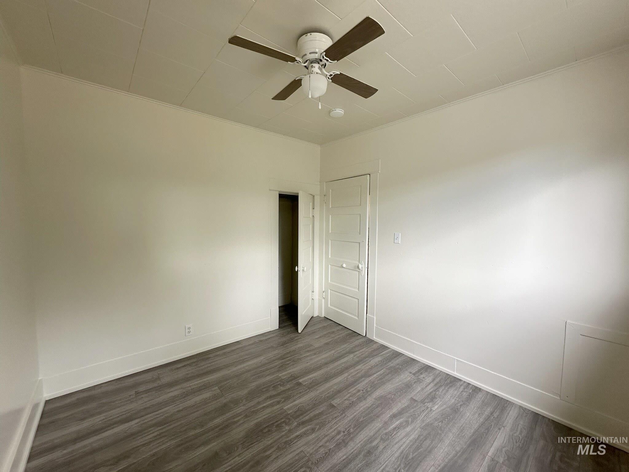 Room featuring wood-finish flooring, white walls, and a ceiling fan with light fixture