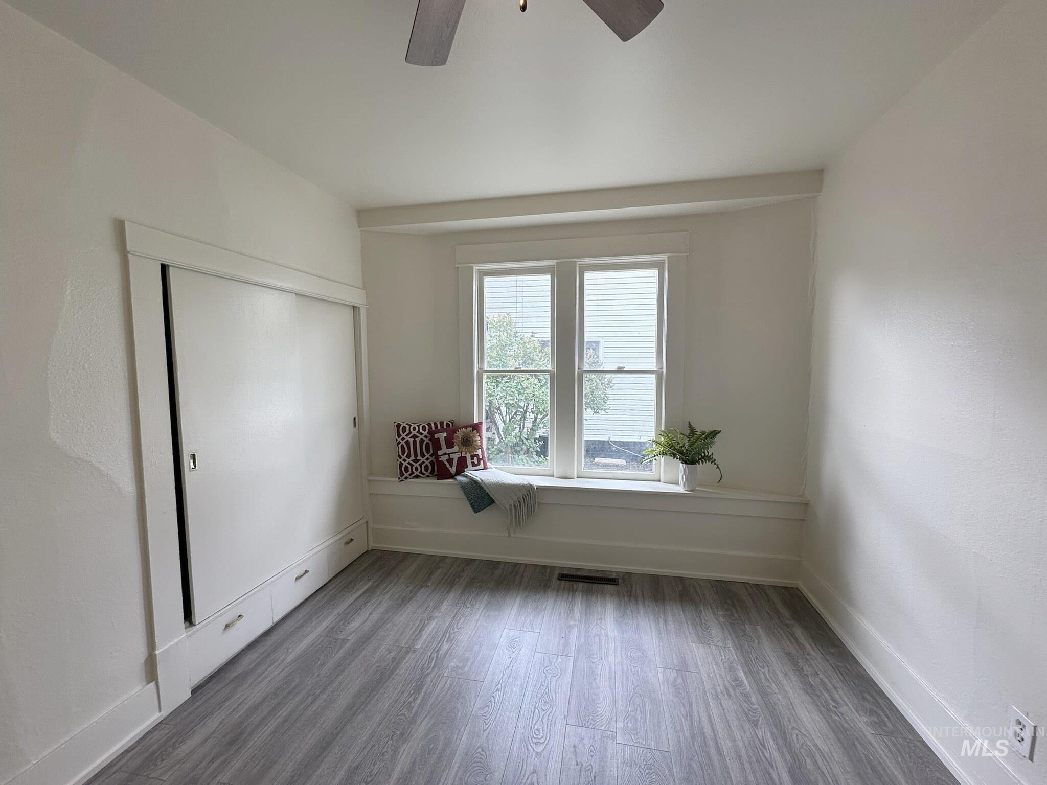 Spacious room featuring wood-finish flooring, a built-in window seat, and a built-in wall unit with integrated drawers