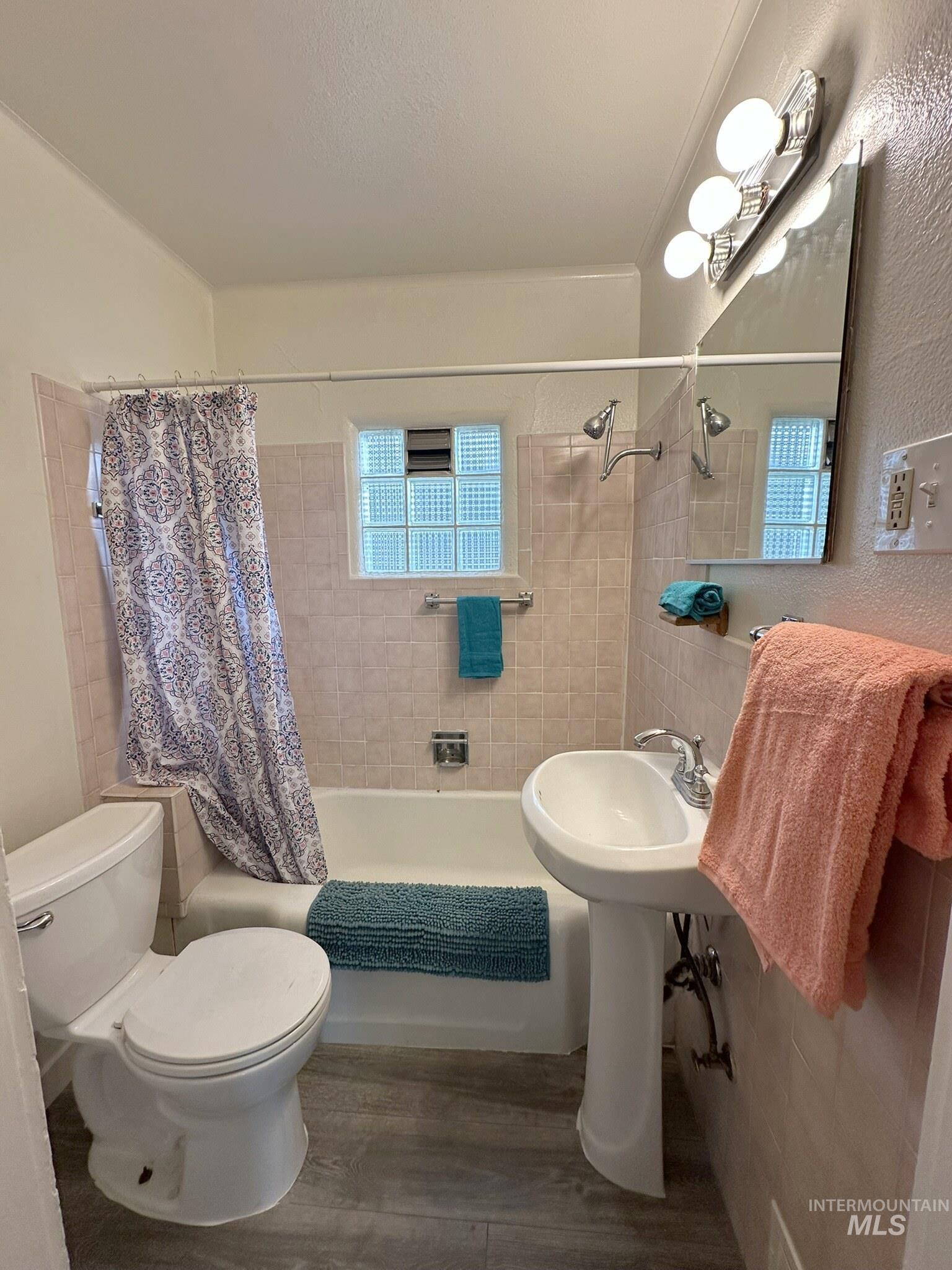 Bathroom featuring a white pedestal sink, ceramic tile walls, and a bathtub with an integrated shower