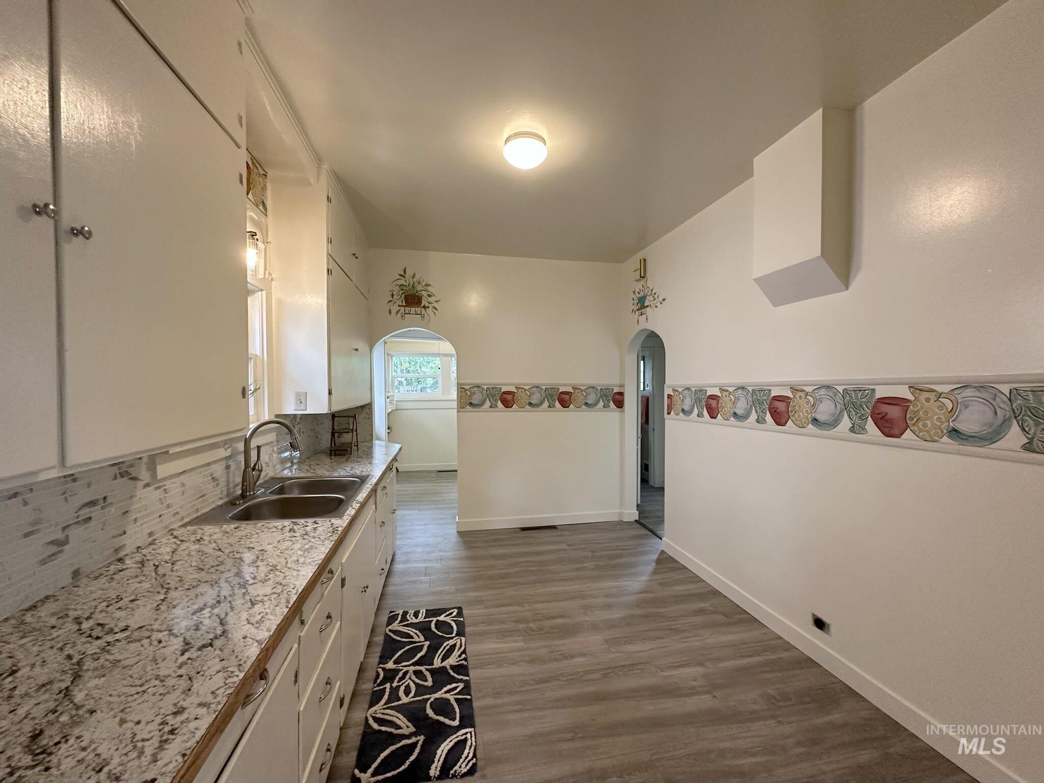Kitchen featuring white cabinetry, a dual basin stainless steel sink with a gooseneck faucet, light-toned granite countertops, and a white tiled backsplash