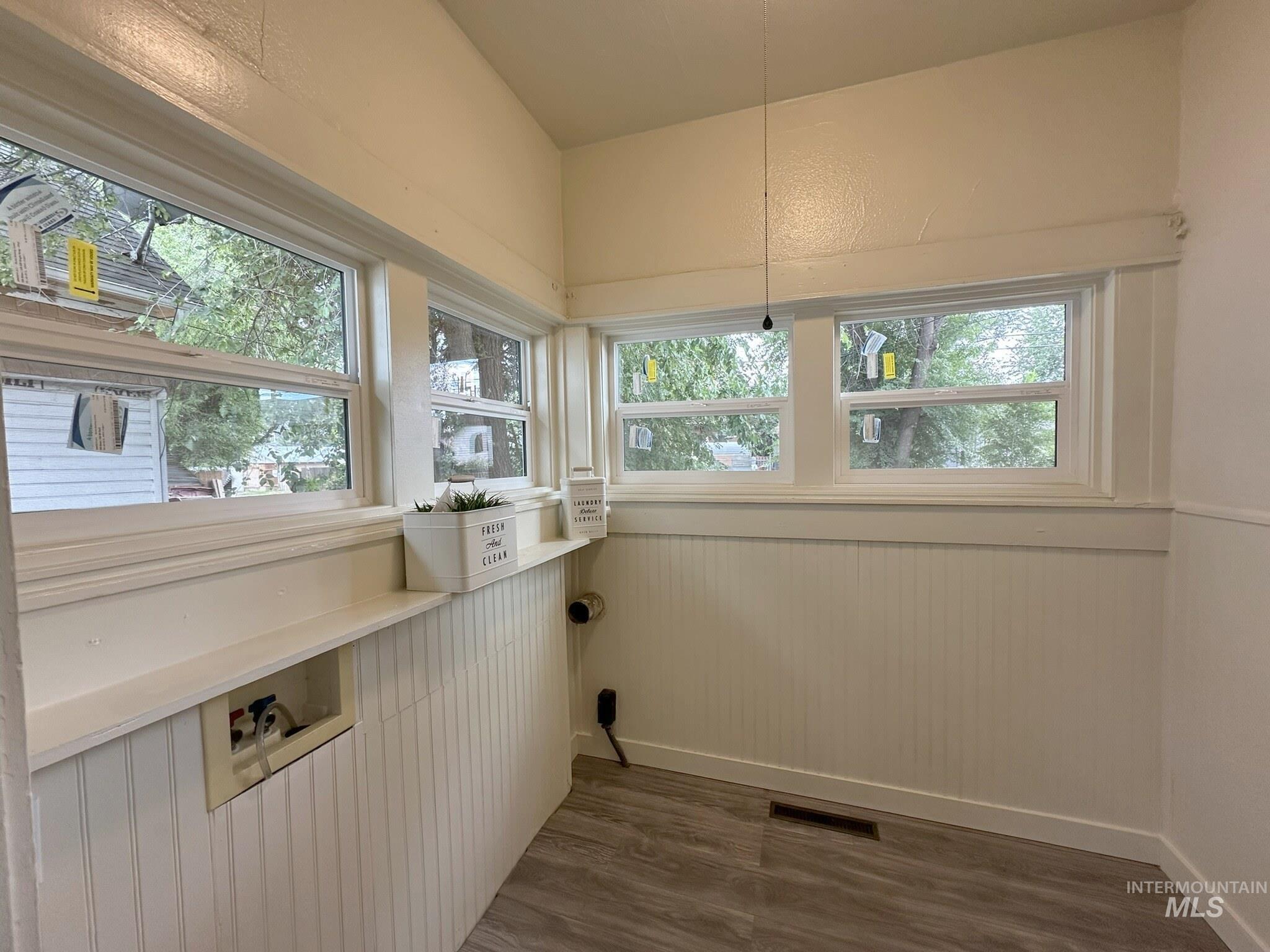 Utility room featuring light wood-finish flooring, white beadboard wainscoting, and multiple windows with white trim