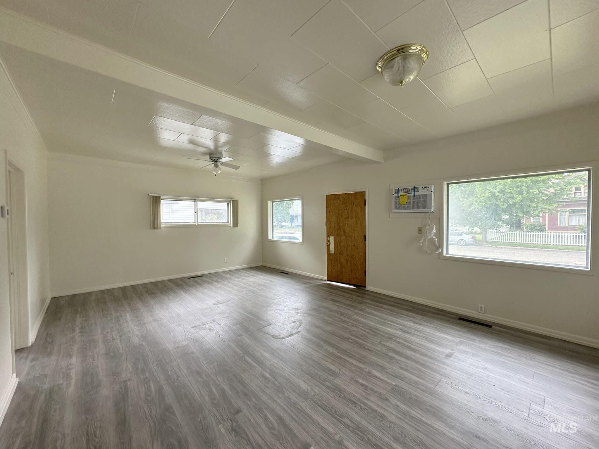 Spacious room featuring wood-finish flooring, multiple windows, a ceiling fan, and an air conditioning unit
