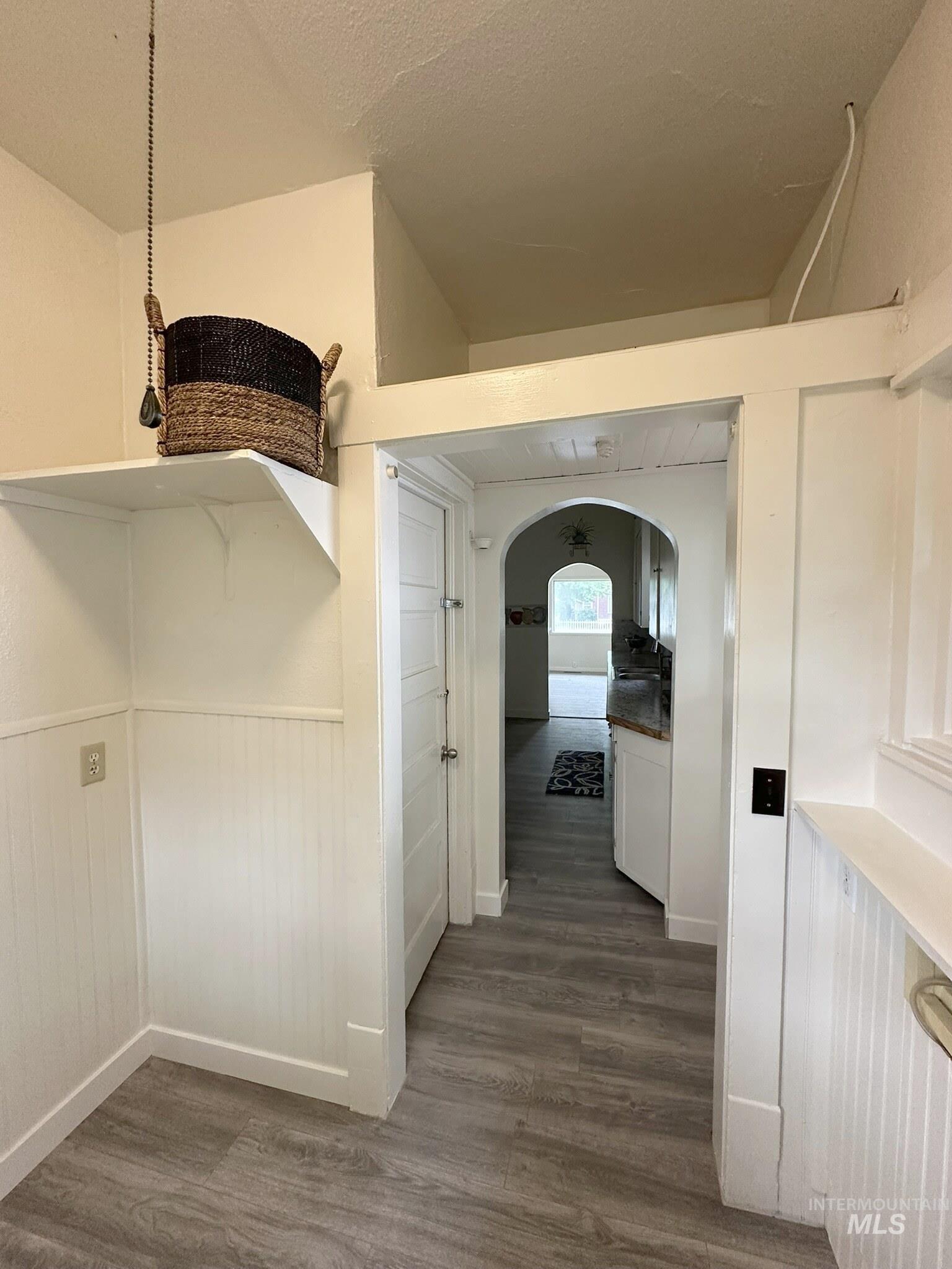 Interior hallway featuring wood-finish flooring, white beadboard wainscoting, and a built-in shelf
