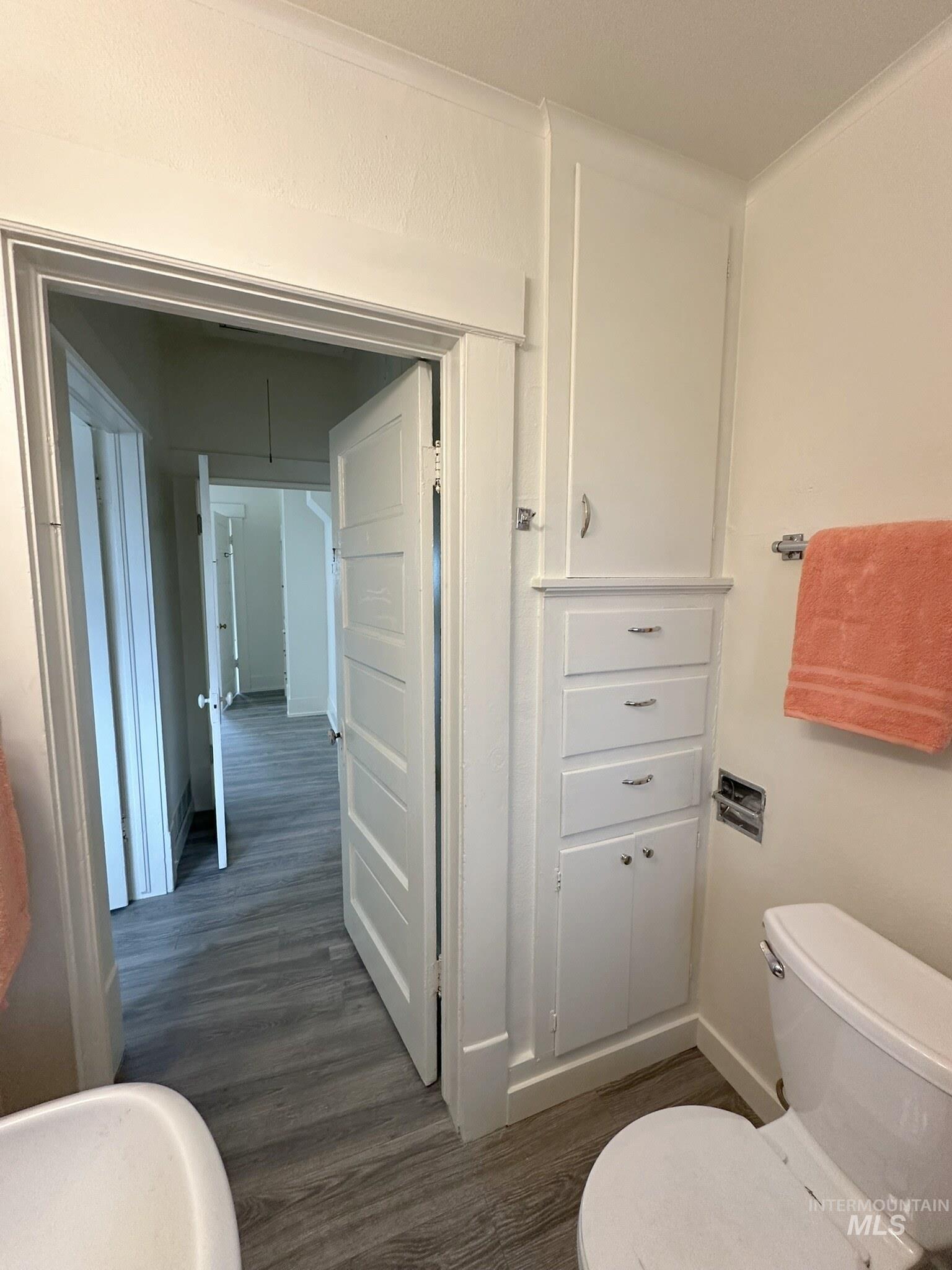 Bathroom featuring a white toilet, built-in vertical cabinetry with multiple drawers and a lower cabinet, and wood-finish flooring