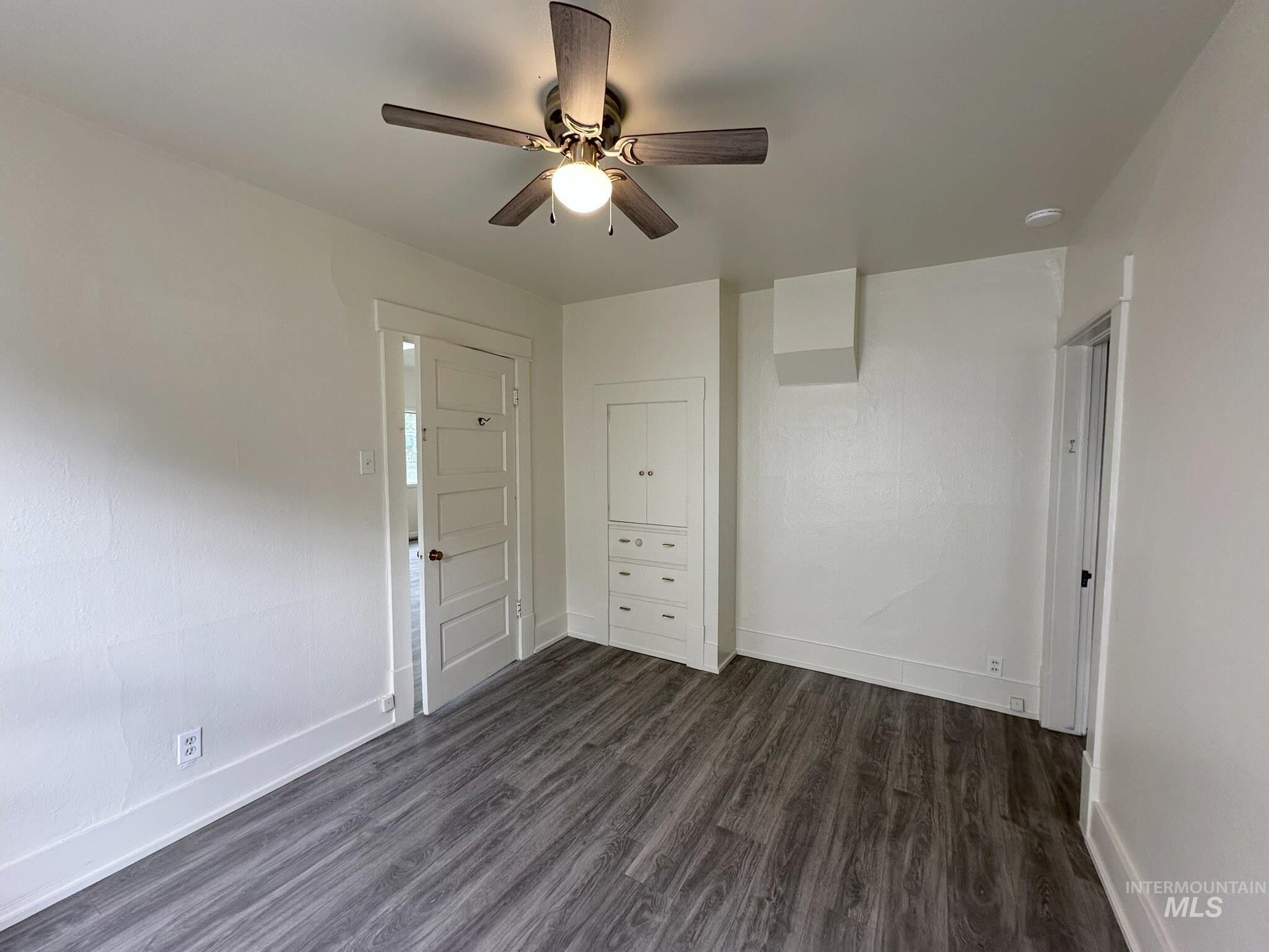 Room featuring wood-finish flooring, a ceiling fan, and built-in cabinetry with drawers