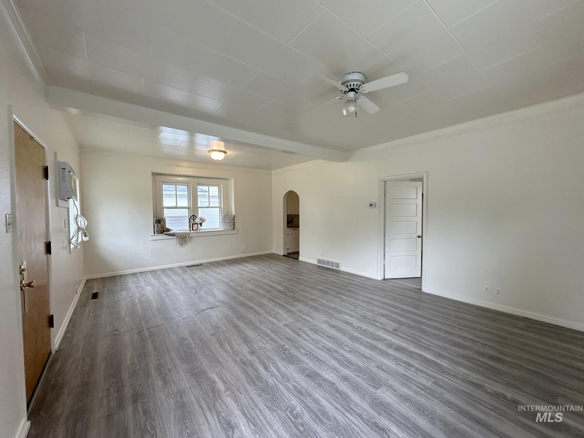 Spacious room featuring wood-finish flooring, white walls, and a ceiling fan