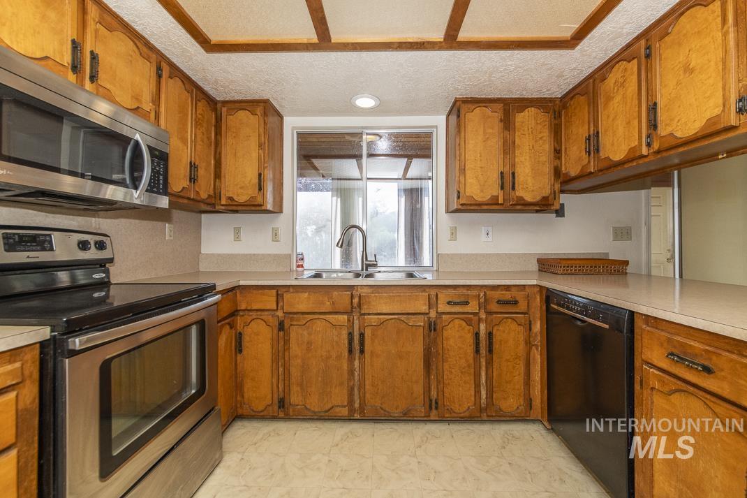 Kitchen with appliances with stainless steel finishes, brown cabinetry, light countertops, and a textured ceiling