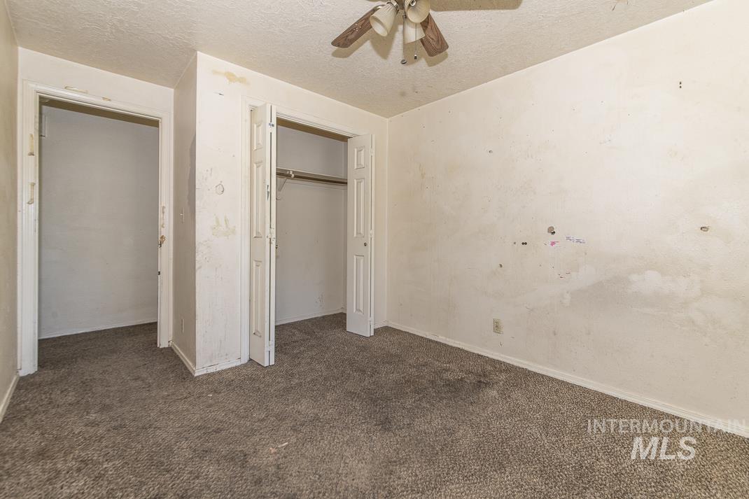 Unfurnished bedroom with dark colored carpet, a textured ceiling, a closet, and a ceiling fan