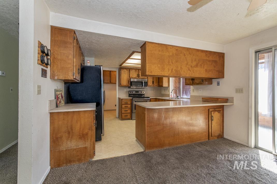 Kitchen featuring brown cabinets, a peninsula, light countertops, a textured ceiling, and appliances with stainless steel finishes