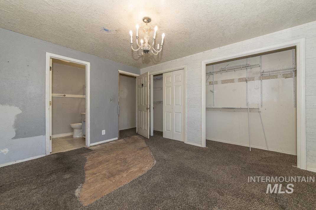 Unfurnished bedroom with a textured ceiling, multiple closets, ensuite bath, carpet floors, and a chandelier