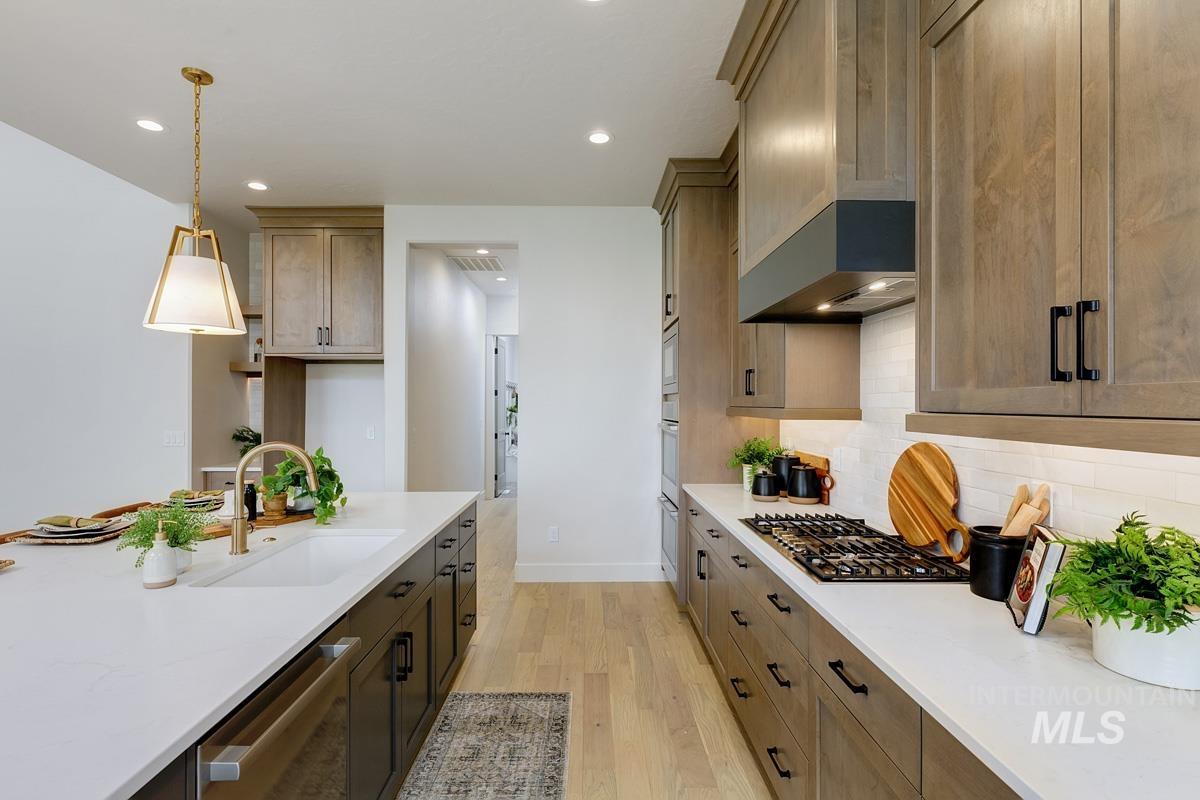 Kitchen with decorative light fixtures, light wood-style flooring, stainless steel appliances, light stone counters, and backsplash