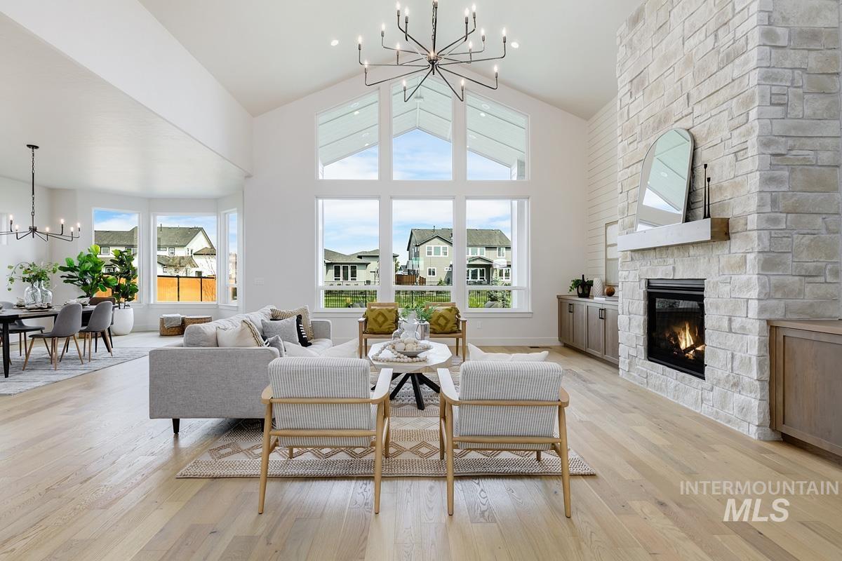 Living room featuring a chandelier, light wood-type flooring, a stone fireplace, and a high ceiling
