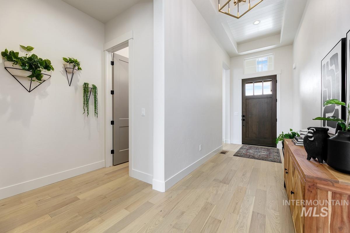 Foyer entrance featuring light wood finished floors, hanging lights, and a raised ceiling