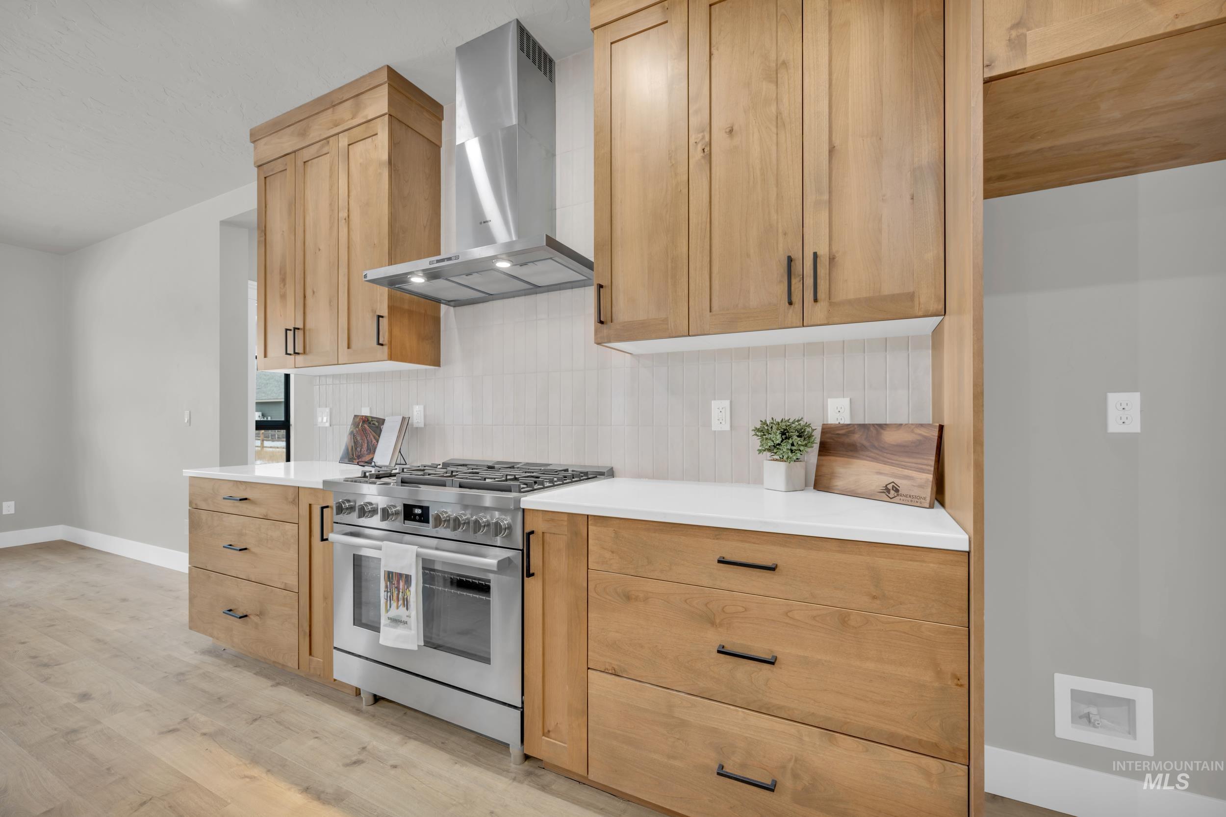 Kitchen featuring wall chimney range hood, stainless steel gas range, light brown cabinets, and decorative backsplash