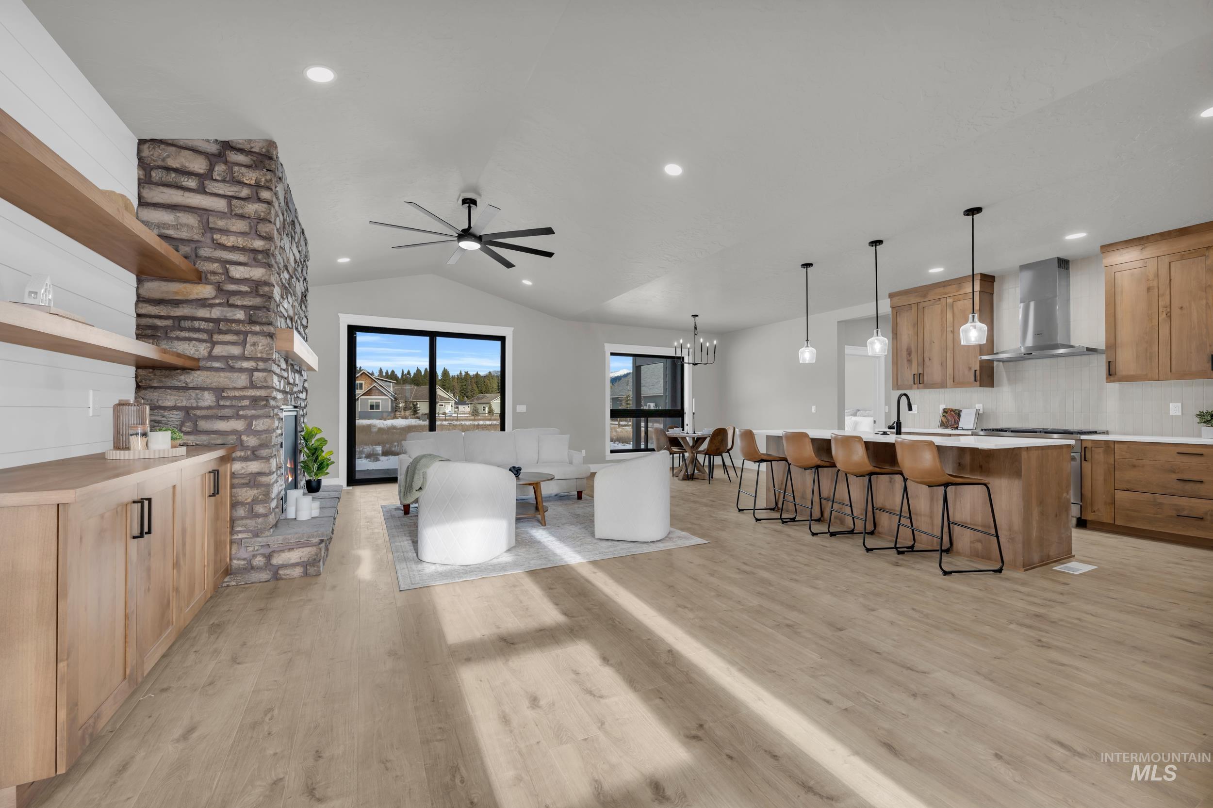 Kitchen featuring open shelves, a chandelier, lofted ceiling, a kitchen island with sink, and wall chimney exhaust hood