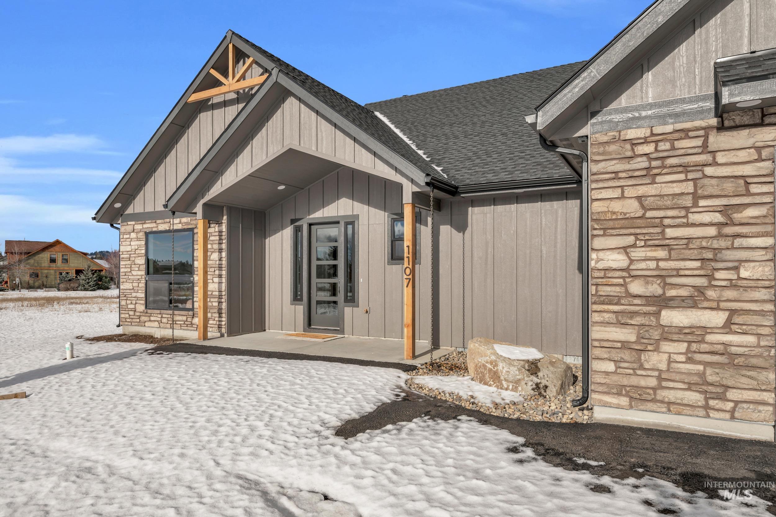 Snow covered property entrance with stone siding and a shingled roof
