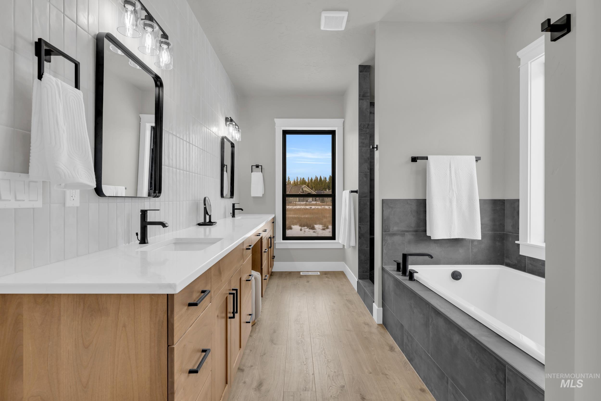 Full bath featuring a bath, double vanity, light wood-style flooring, and decorative backsplash