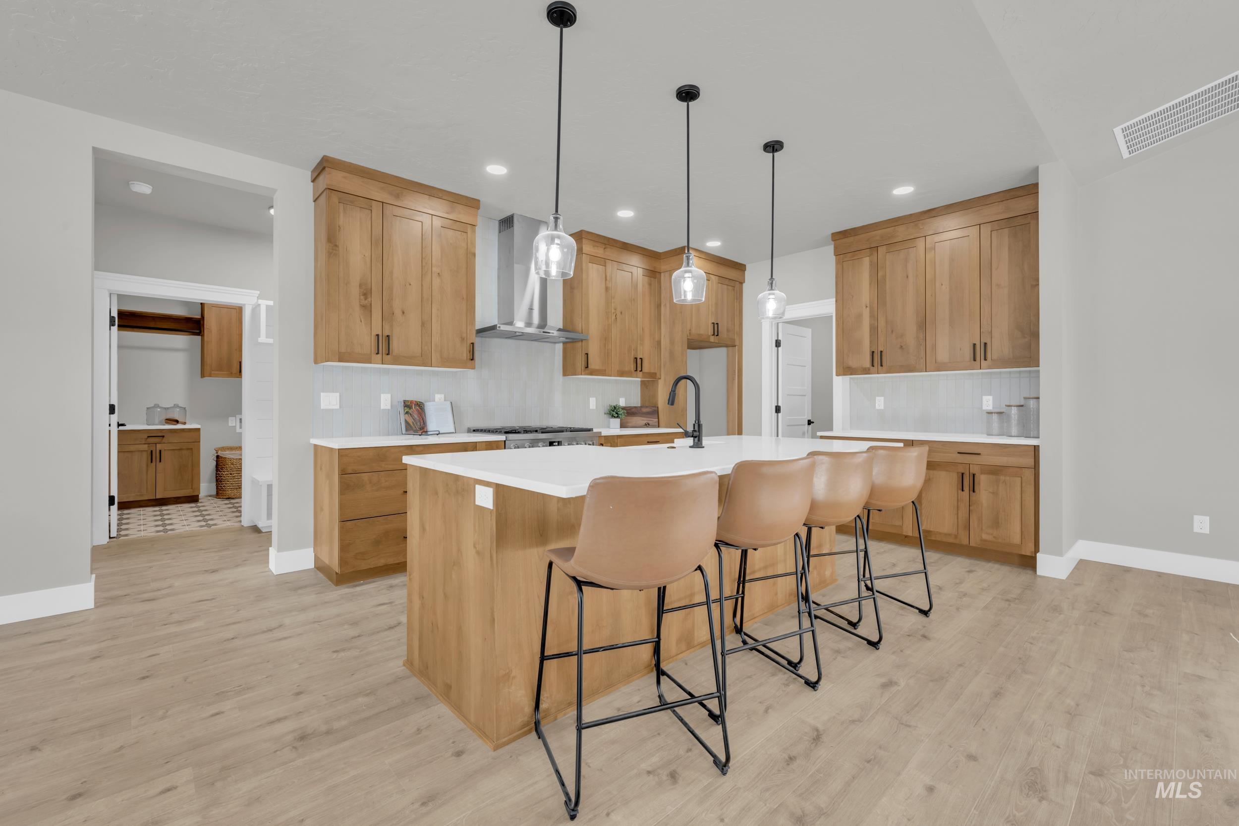 Kitchen featuring a breakfast bar area, decorative light fixtures, a kitchen island with sink, wall chimney exhaust hood, and tasteful backsplash