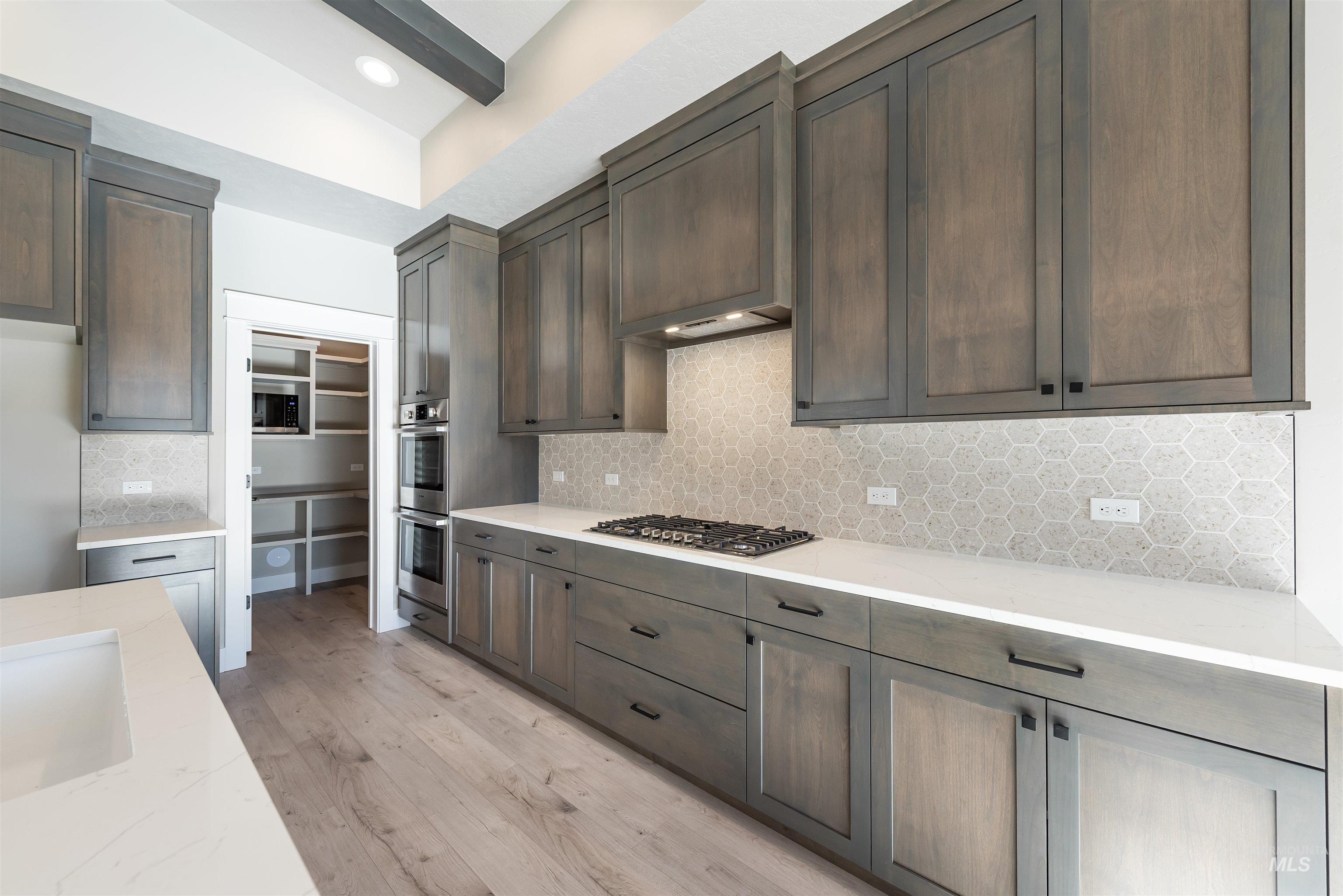 Kitchen featuring light stone counters, decorative backsplash, light wood finished floors, and stainless steel appliances