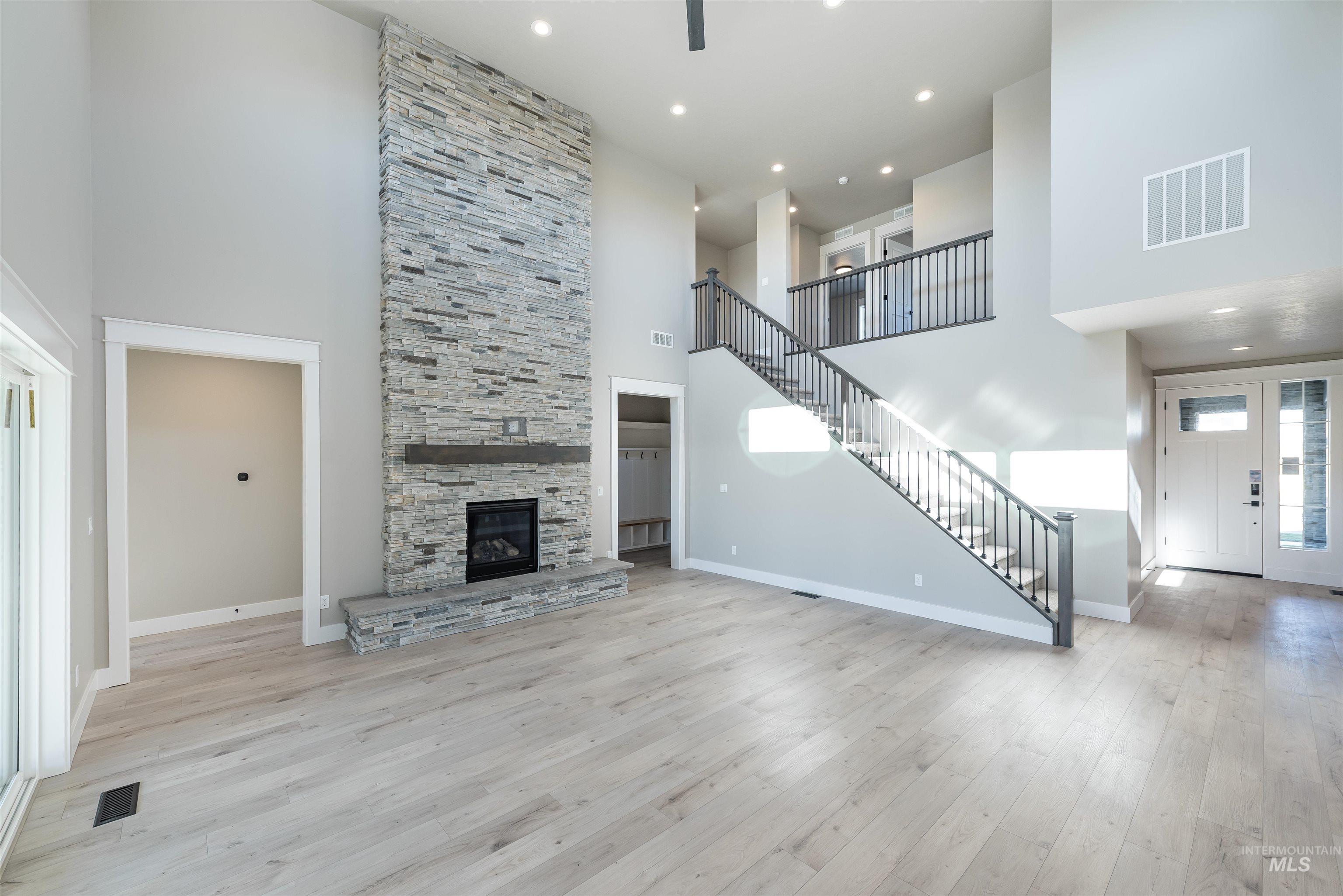 Unfurnished living room with stairway, a towering ceiling, light wood-style floors, recessed lighting, and a stone fireplace