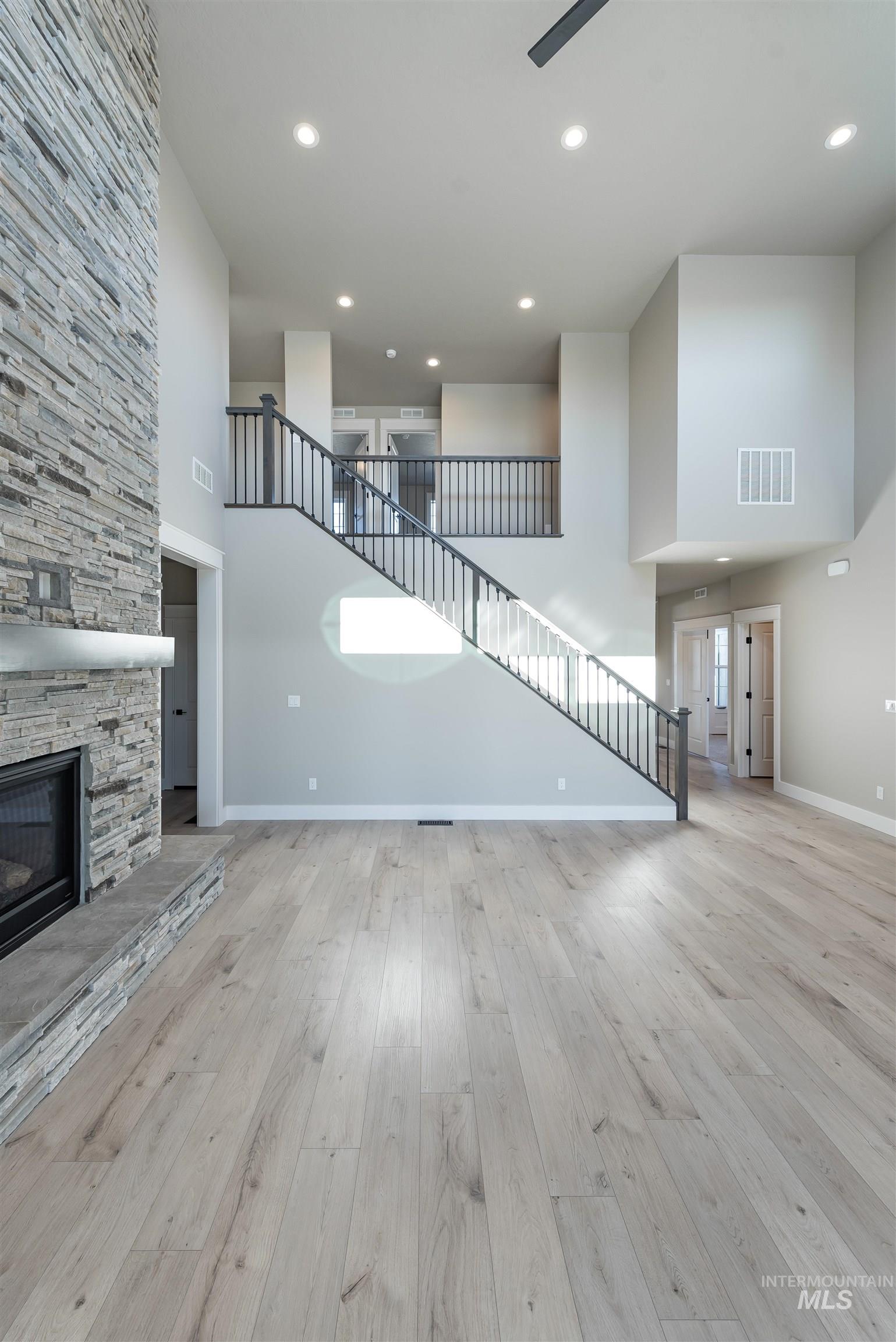 Unfurnished living room with stairs, a towering ceiling, a stone fireplace, light wood finished floors, and recessed lighting