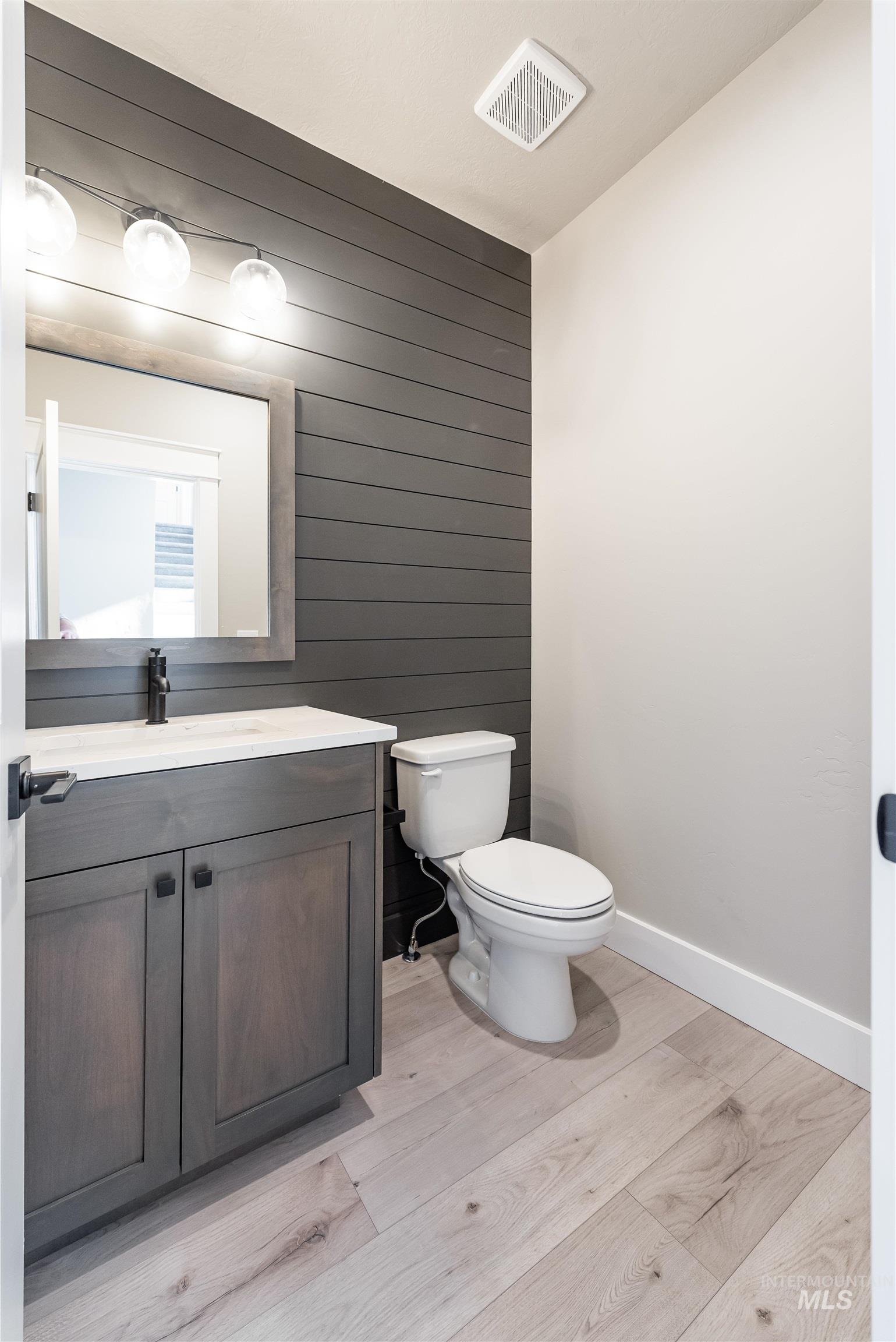 Bathroom featuring wooden walls, vanity, light wood-style flooring, and an accent wall