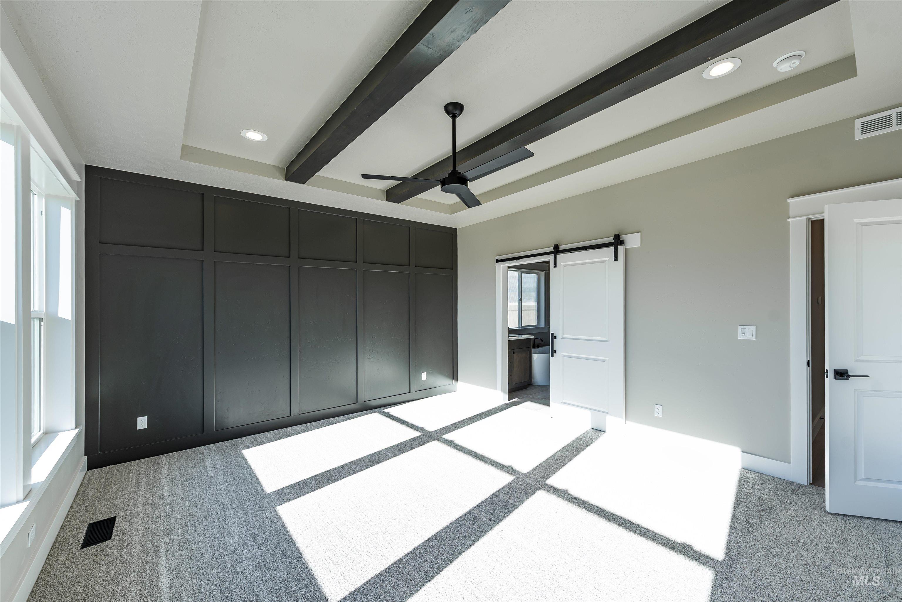 Unfurnished bedroom featuring a barn door, recessed lighting, ensuite bathroom, light carpet, and beam ceiling