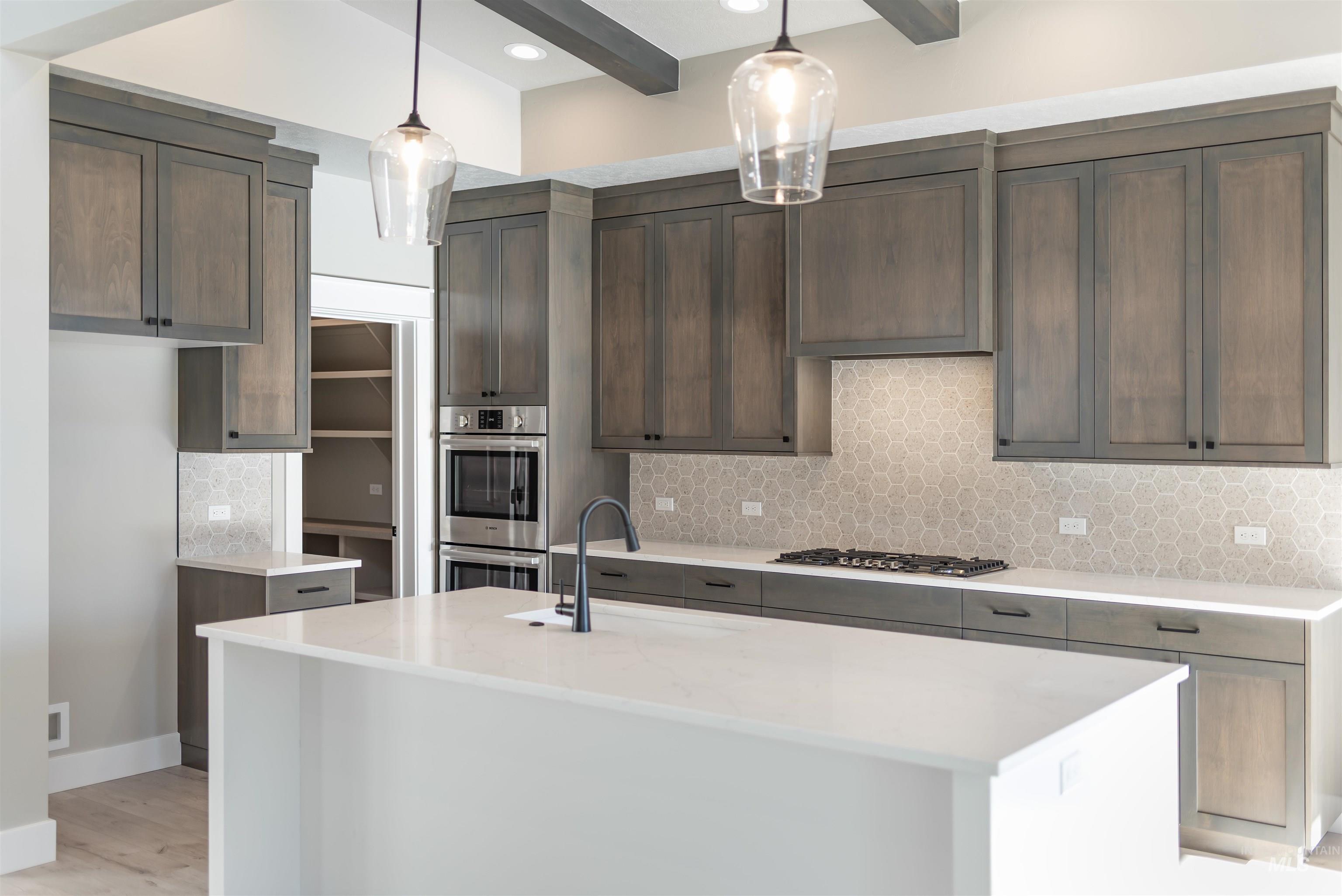 Kitchen with decorative backsplash, a kitchen island with sink, light stone countertops, stainless steel appliances, and beamed ceiling