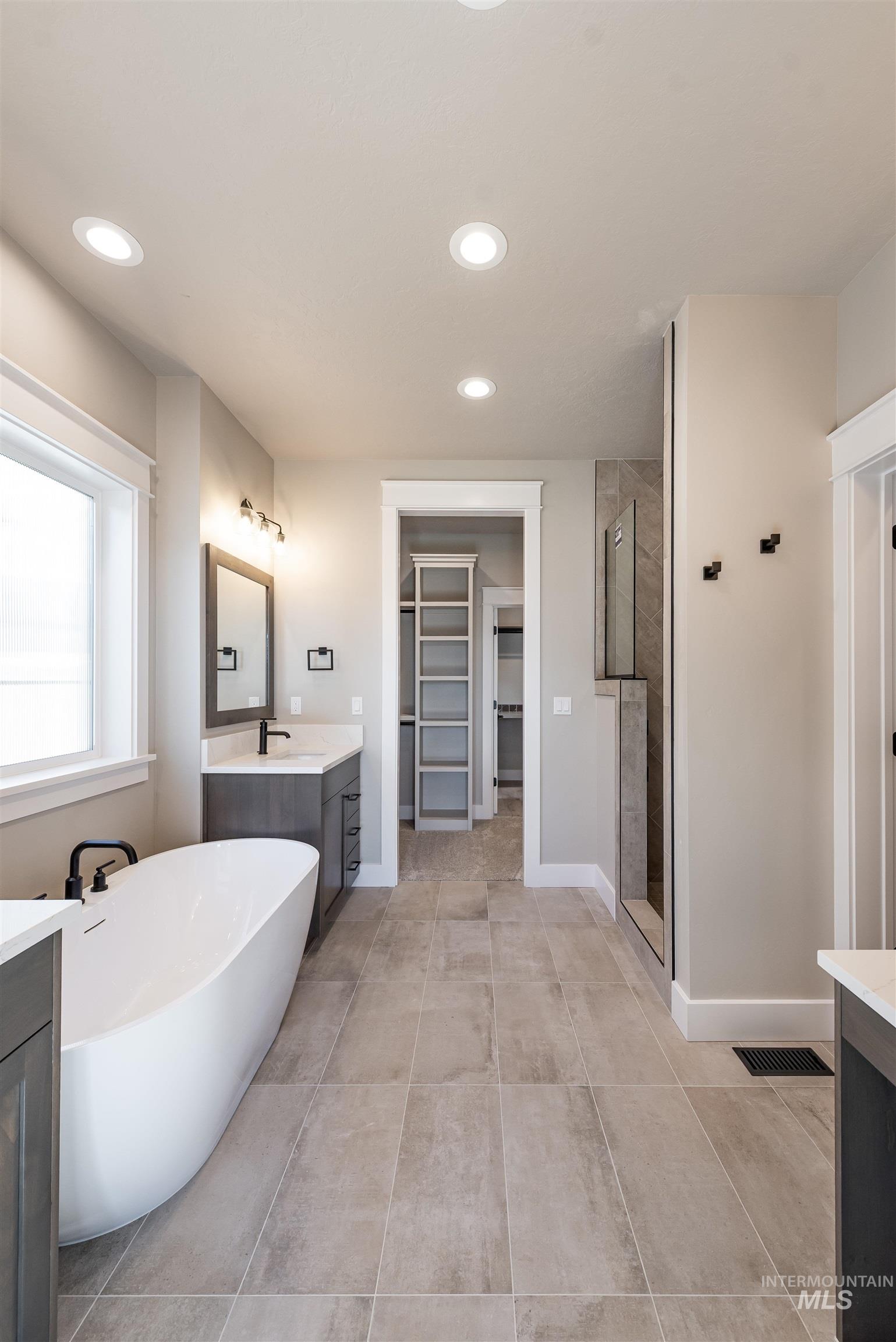 Full bathroom with a spacious closet, two vanities, a freestanding bath, recessed lighting, and a stall shower