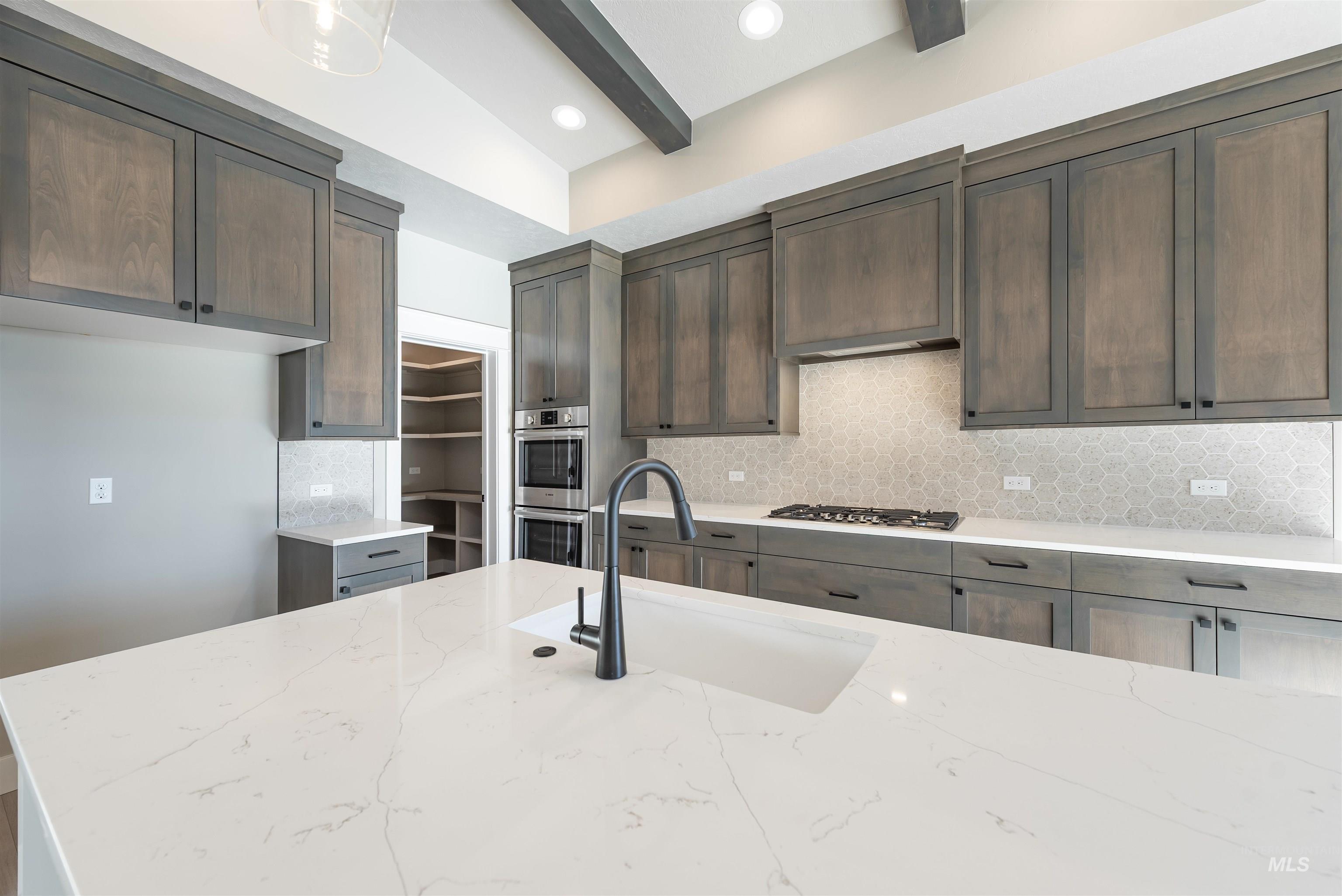 Kitchen with tasteful backsplash, light stone countertops, beam ceiling, stainless steel appliances, and dark brown cabinets