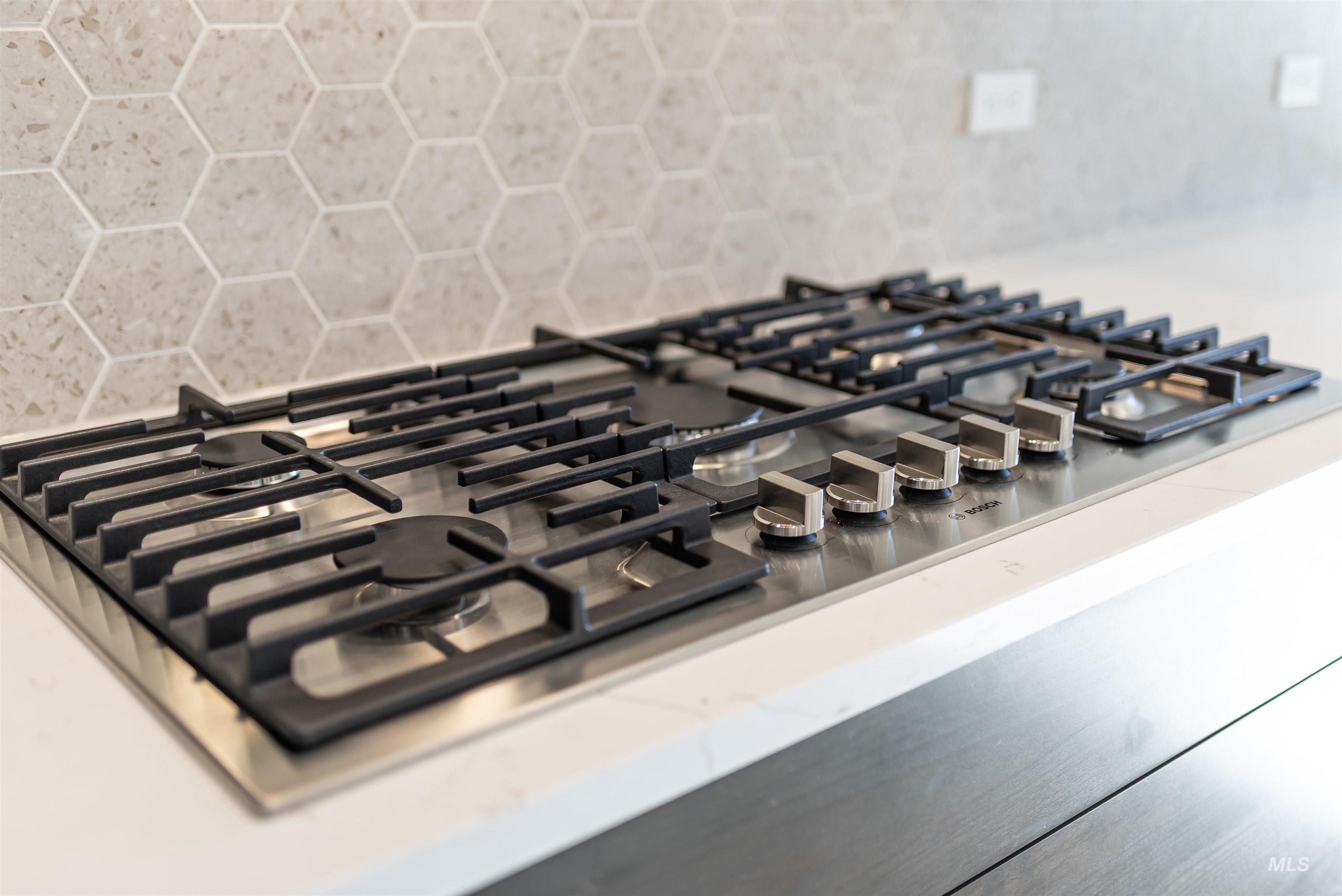 Kitchen view of stainless steel gas cooktop, backsplash, and light stone counters