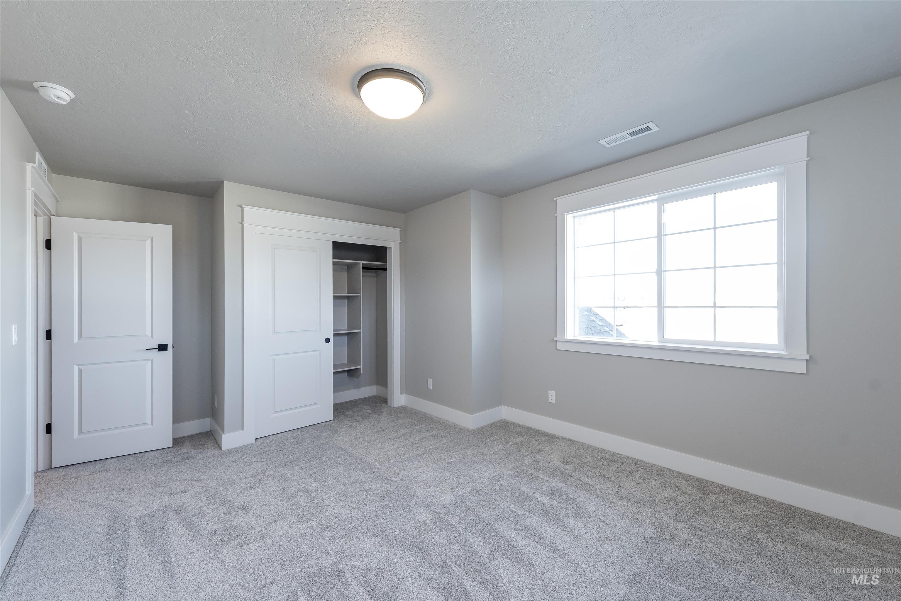 Unfurnished bedroom featuring a closet, light colored carpet, and a textured ceiling