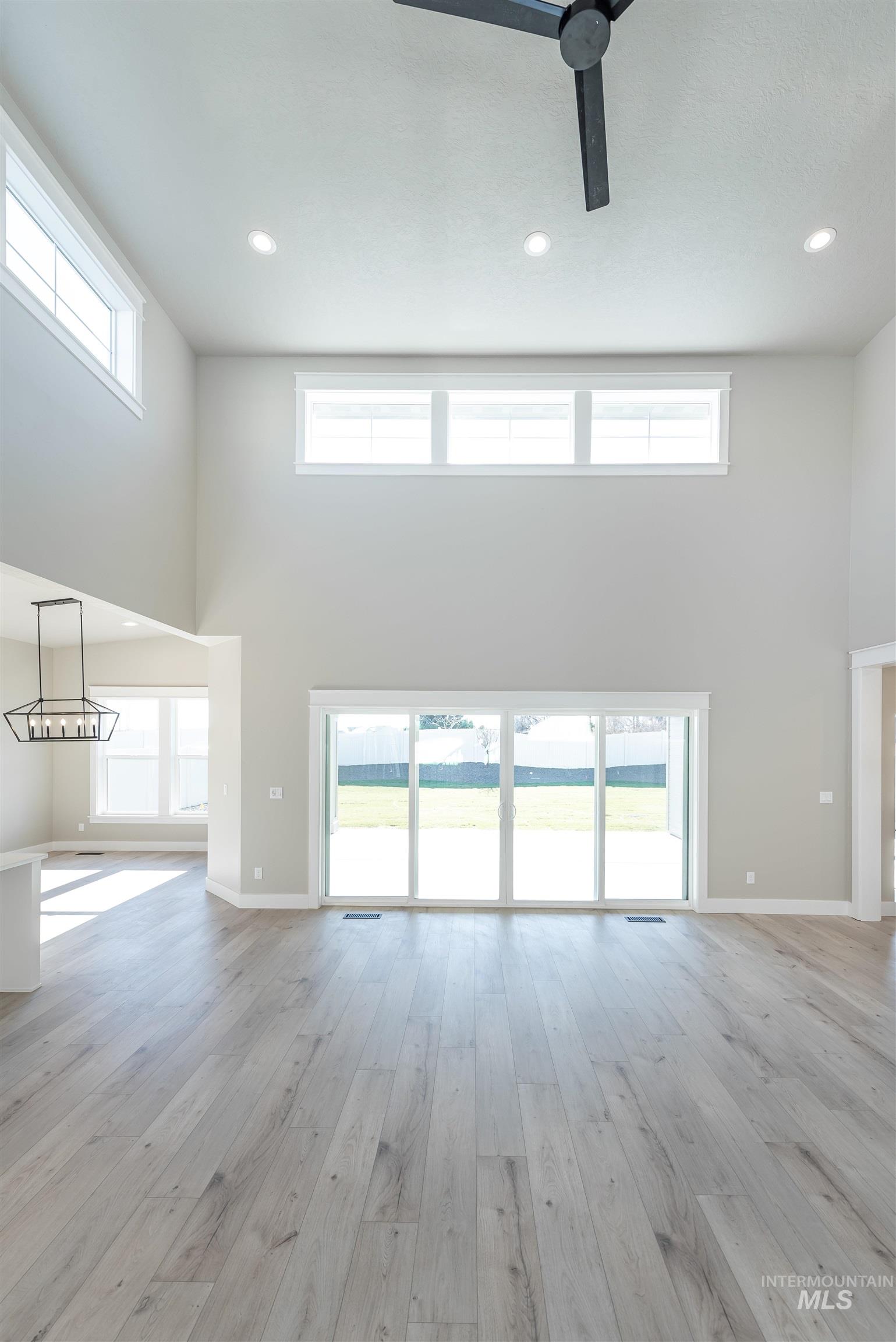Unfurnished living room featuring a high ceiling, recessed lighting, light wood-type flooring, plenty of natural light, and a ceiling fan