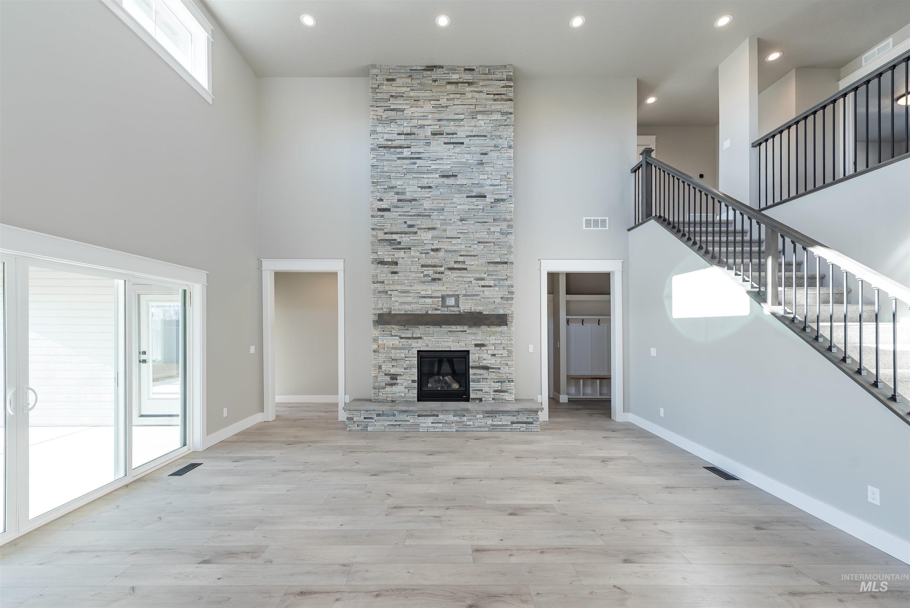 Unfurnished living room featuring a towering ceiling, stairway, light wood-style floors, recessed lighting, and a fireplace