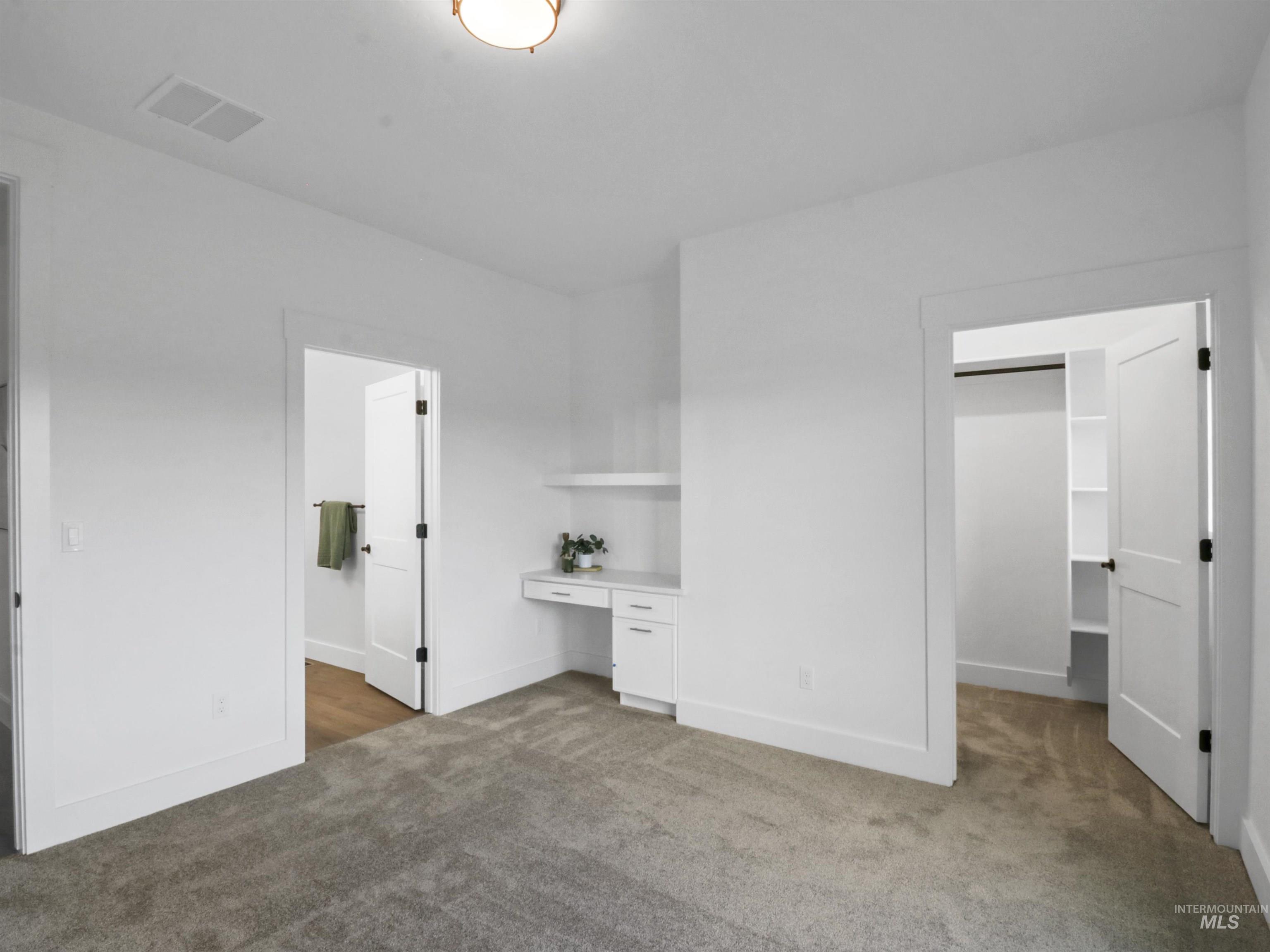 Unfurnished bedroom with built in desk, a spacious closet, and light carpet