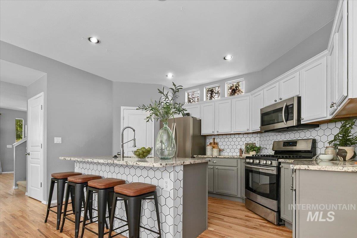 Kitchen with appliances with stainless steel finishes, backsplash, a kitchen breakfast bar, light stone countertops, and recessed lighting
