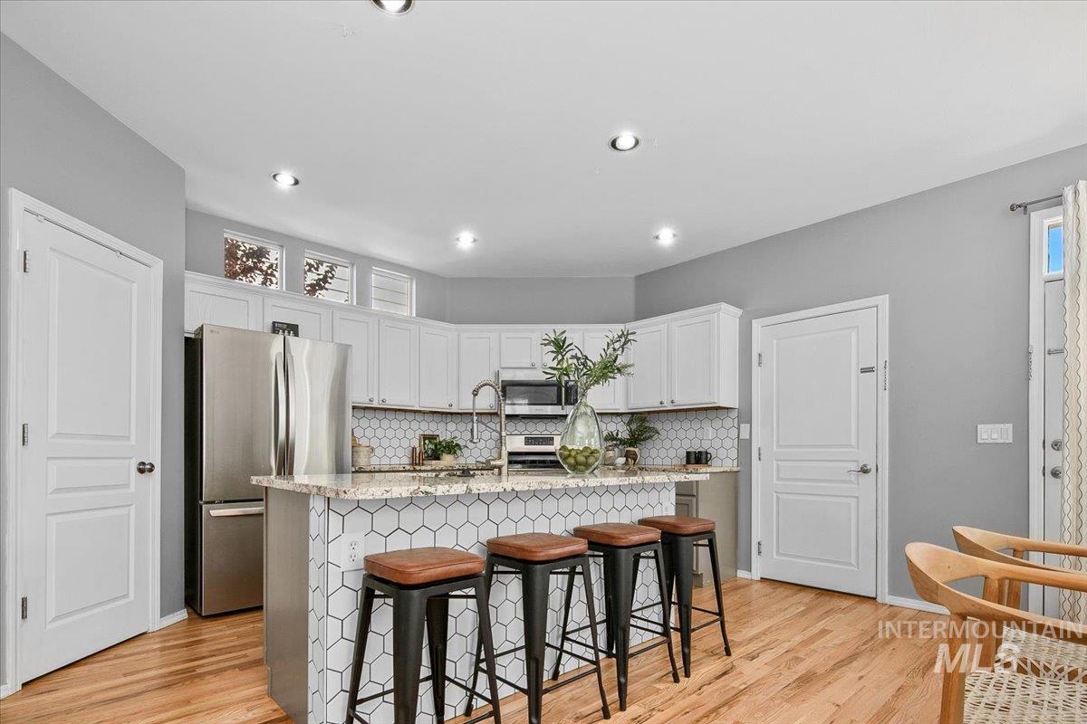 Kitchen featuring a breakfast bar, appliances with stainless steel finishes, backsplash, and a center island with sink