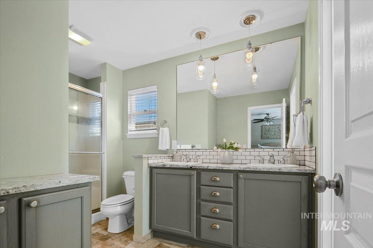 Primary bathroom with double vanity, a shower stall, and decorative backsplash