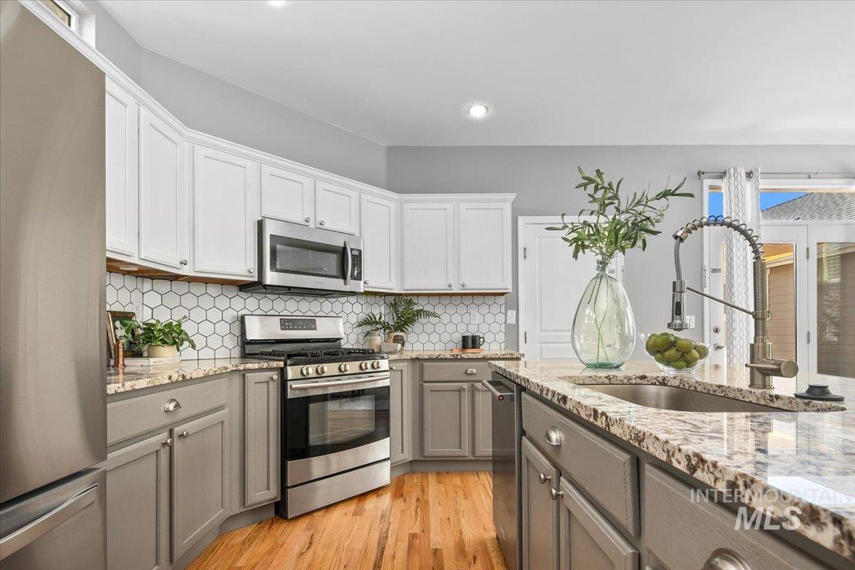 Kitchen with appliances with stainless steel finishes, gray cabinetry, decorative backsplash, light wood finished floors, and recessed lighting
