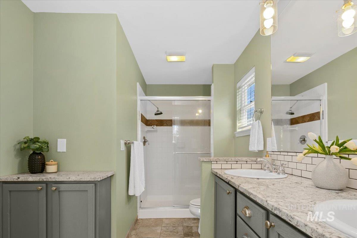 Full bath with a shower stall, double vanity, light tile patterned floors, and decorative backsplash