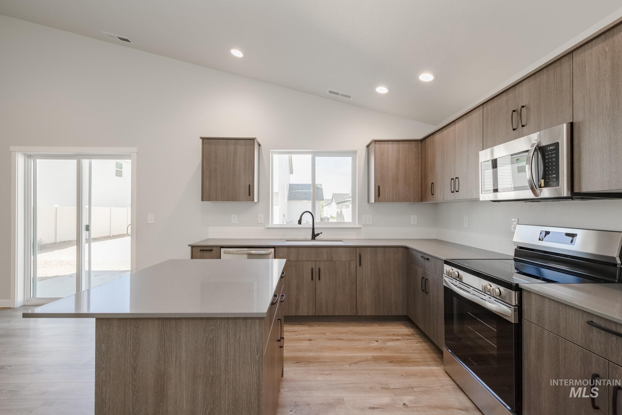 Kitchen with stainless steel appliances, lofted ceiling, light wood-type flooring, a kitchen island, and modern cabinets