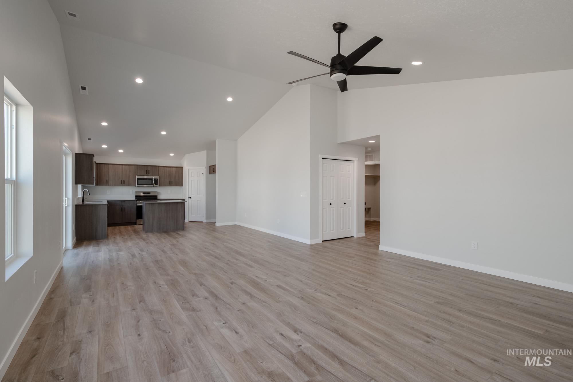 Unfurnished living room with high vaulted ceiling, light wood-style floors, recessed lighting, and a ceiling fan