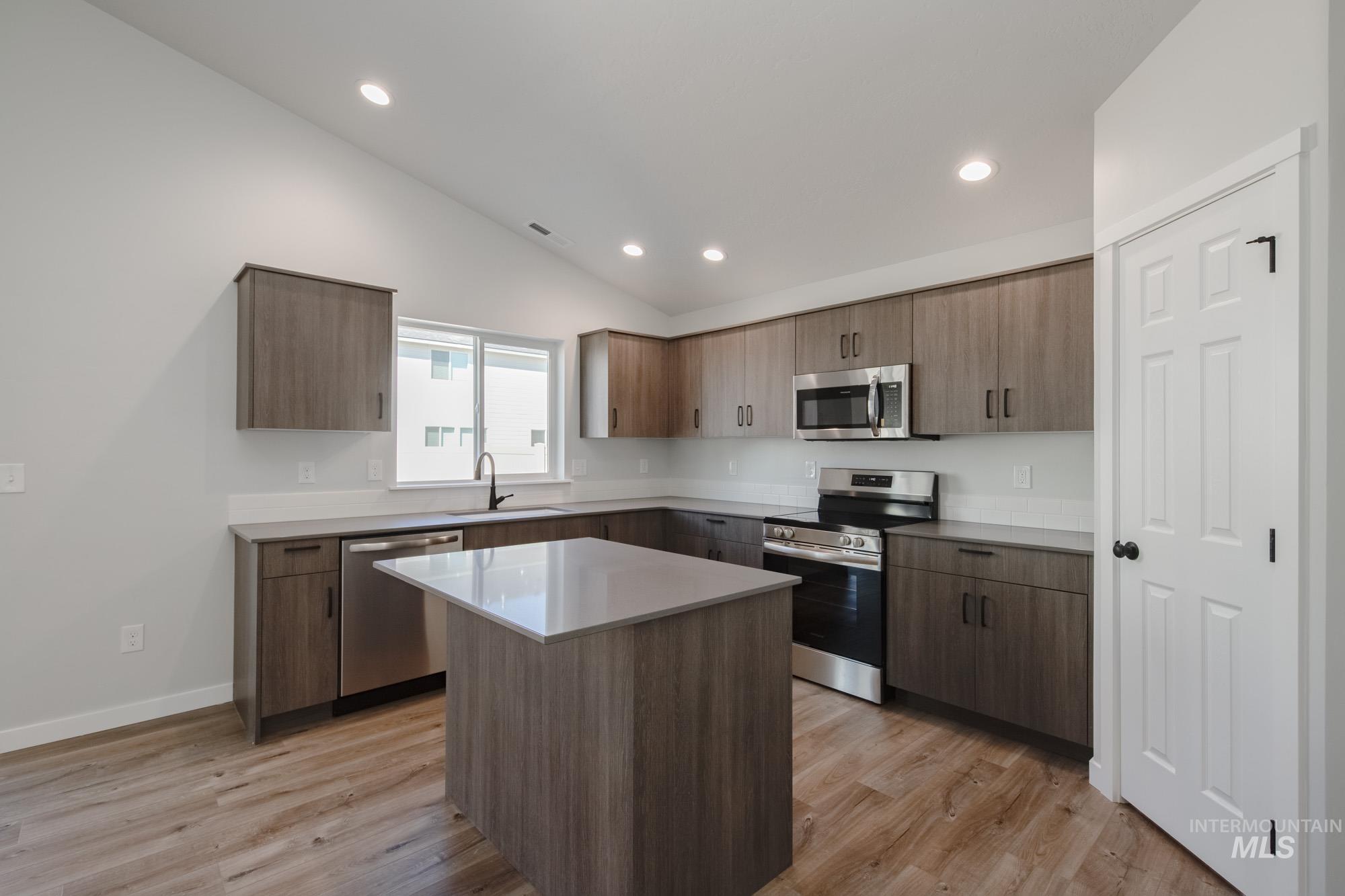Kitchen featuring stainless steel appliances, vaulted ceiling, light wood finished floors, modern cabinets, and recessed lighting